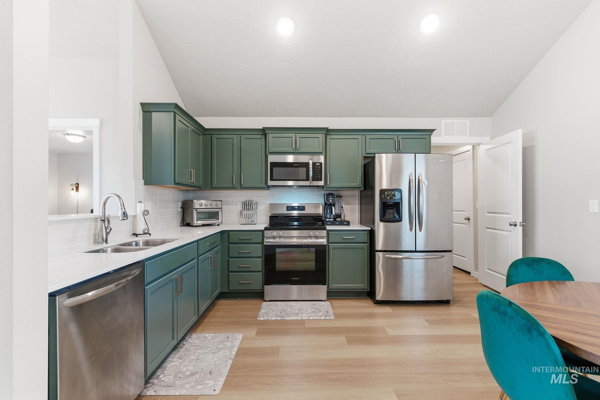 Kitchen with appliances with stainless steel finishes, green cabinets, lofted ceiling, backsplash, and light stone counters
