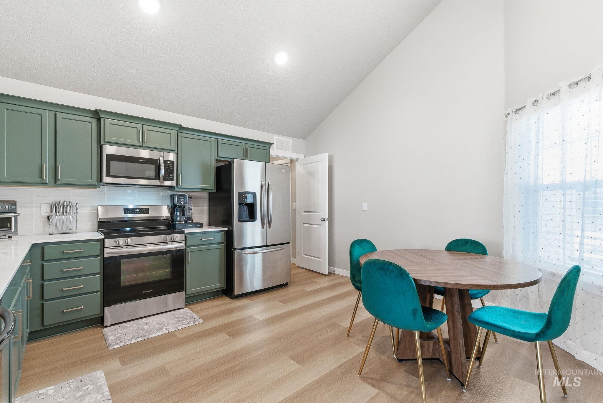 Kitchen with green cabinetry, stainless steel appliances, backsplash, light wood finished floors, and light stone countertops