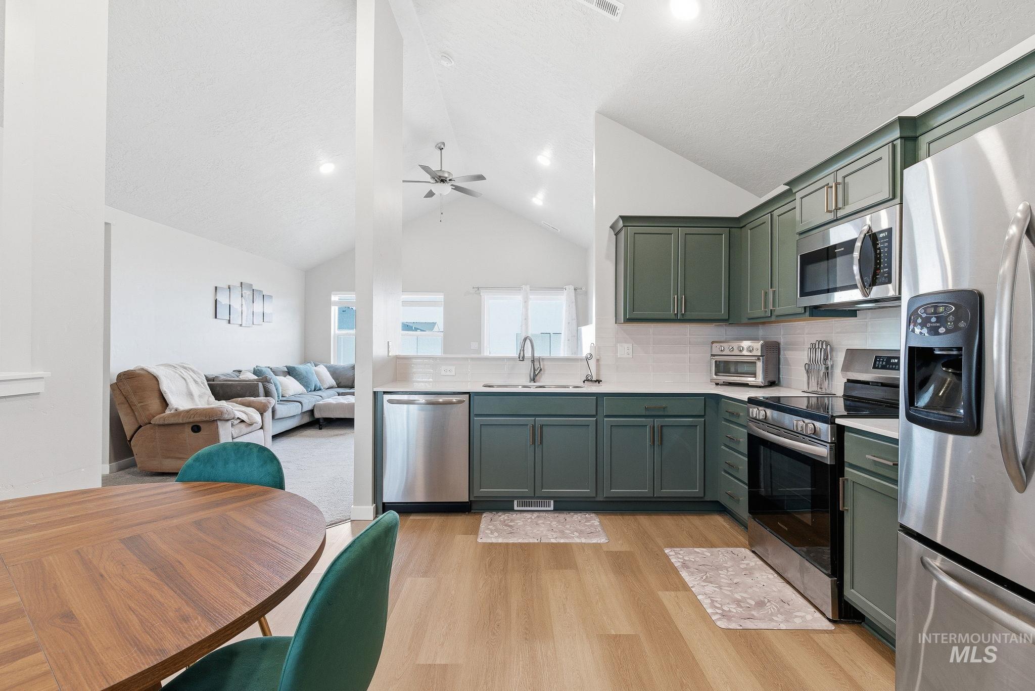 Kitchen featuring appliances with stainless steel finishes, green cabinets, backsplash, lofted ceiling, and open floor plan
