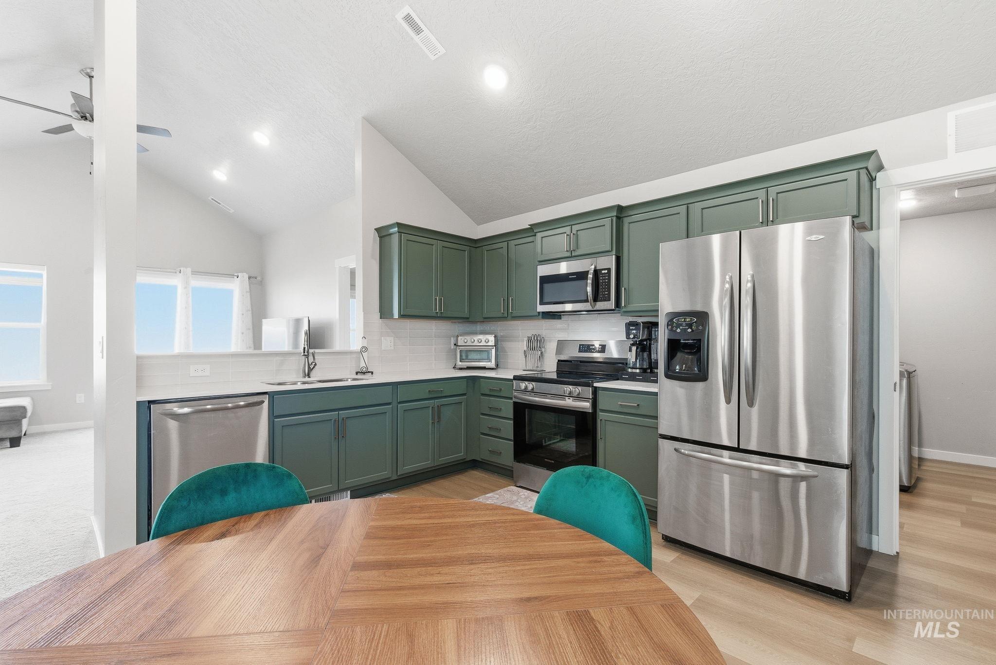 Kitchen featuring stainless steel appliances, decorative backsplash, recessed lighting, green cabinetry, and high vaulted ceiling