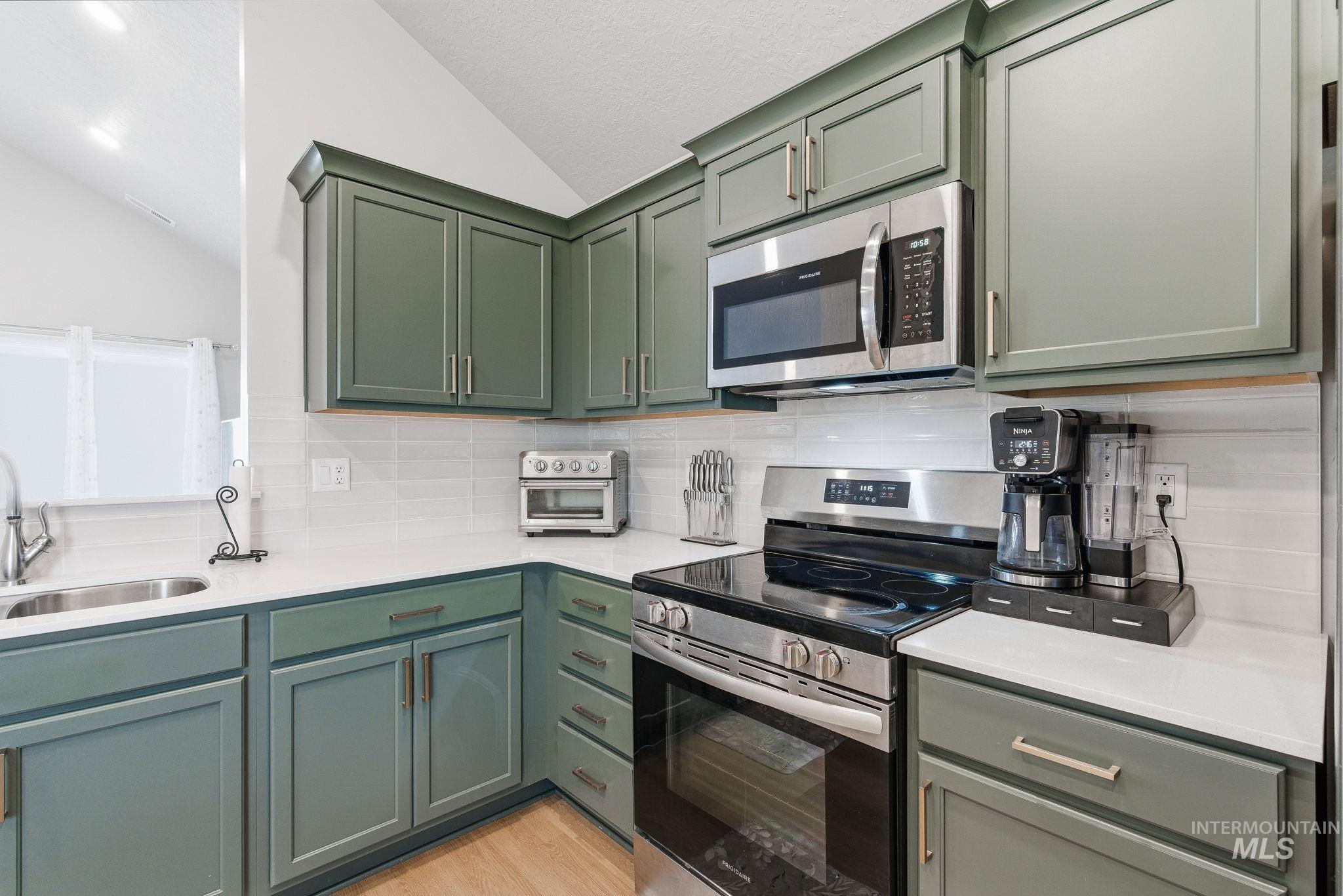 Kitchen with appliances with stainless steel finishes, green cabinets, lofted ceiling, tasteful backsplash, and light stone counters