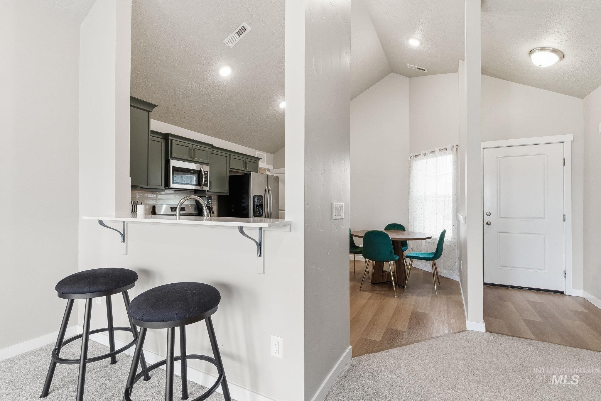 Kitchen with a kitchen bar, appliances with stainless steel finishes, light colored carpet, a peninsula, and backsplash