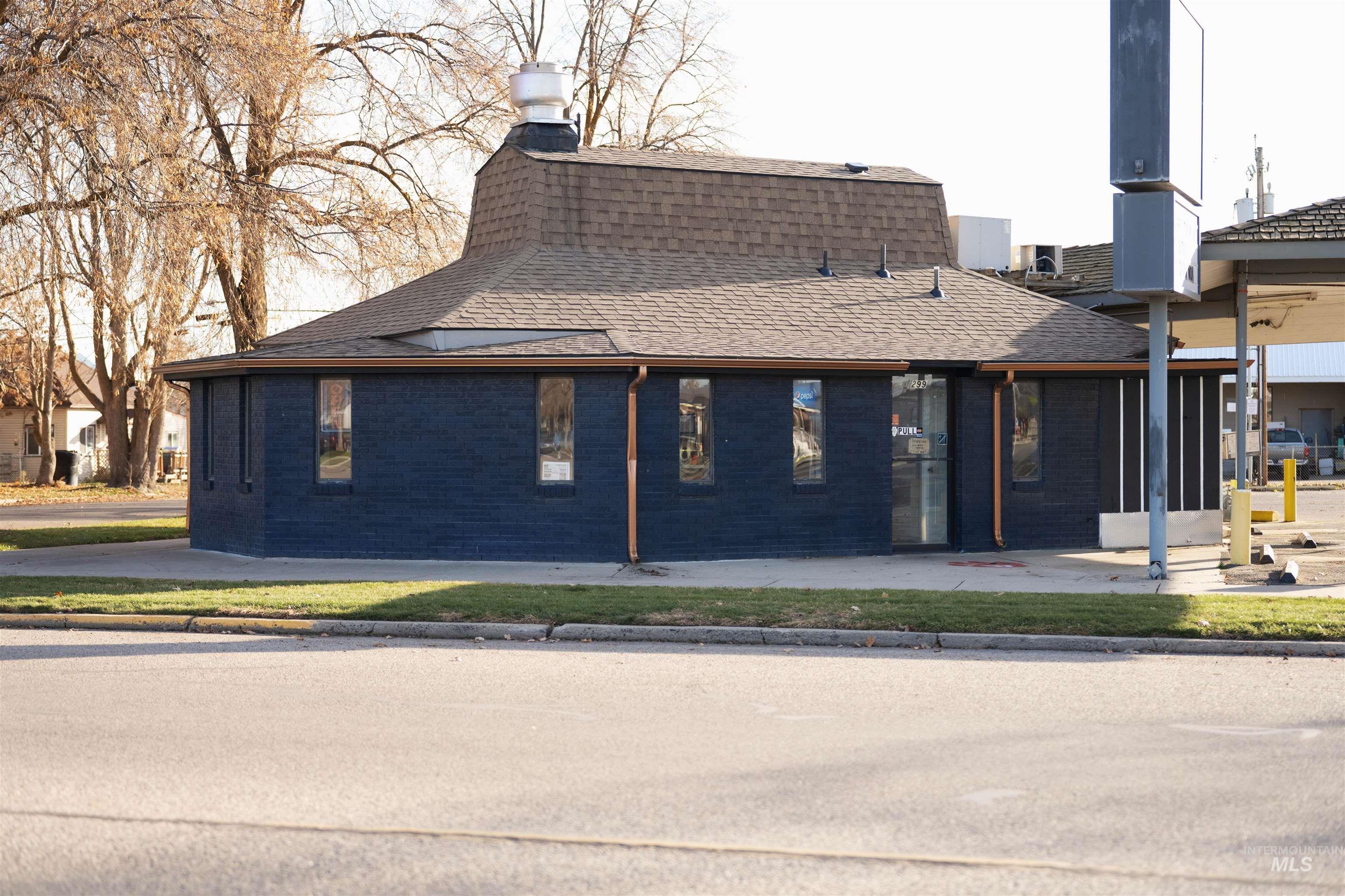 View of side of property featuring a shingled roof, brick siding, a chimney, and a patio