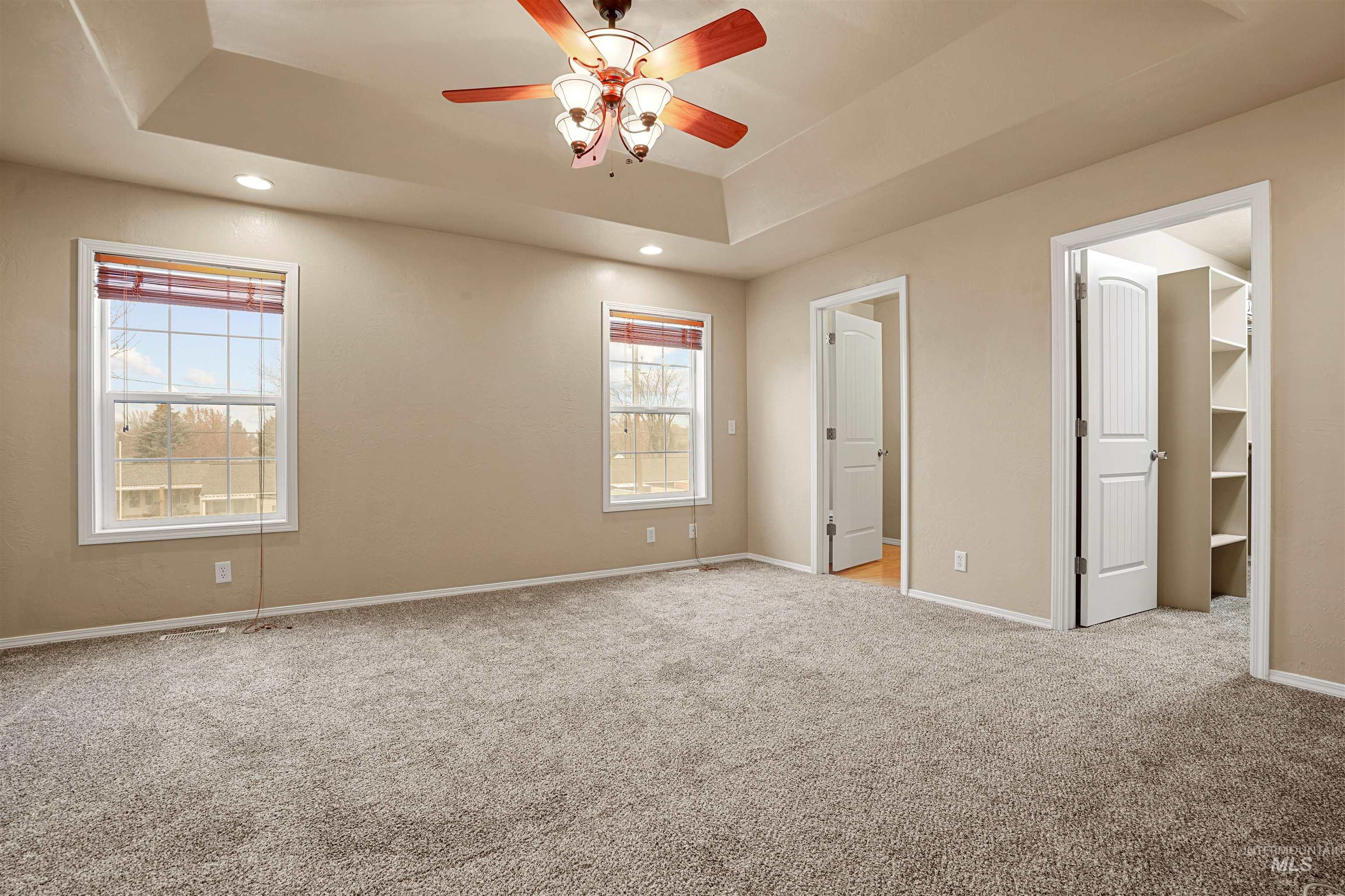 Unfurnished bedroom with a spacious closet, a tray ceiling, light carpet, a ceiling fan, and recessed lighting