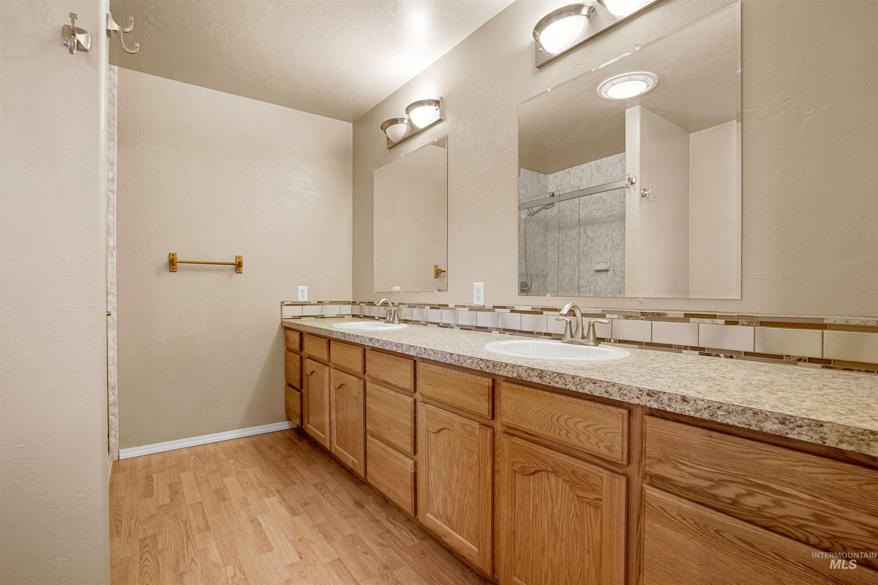 Full bath with double vanity, light wood-type flooring, and a shower stall