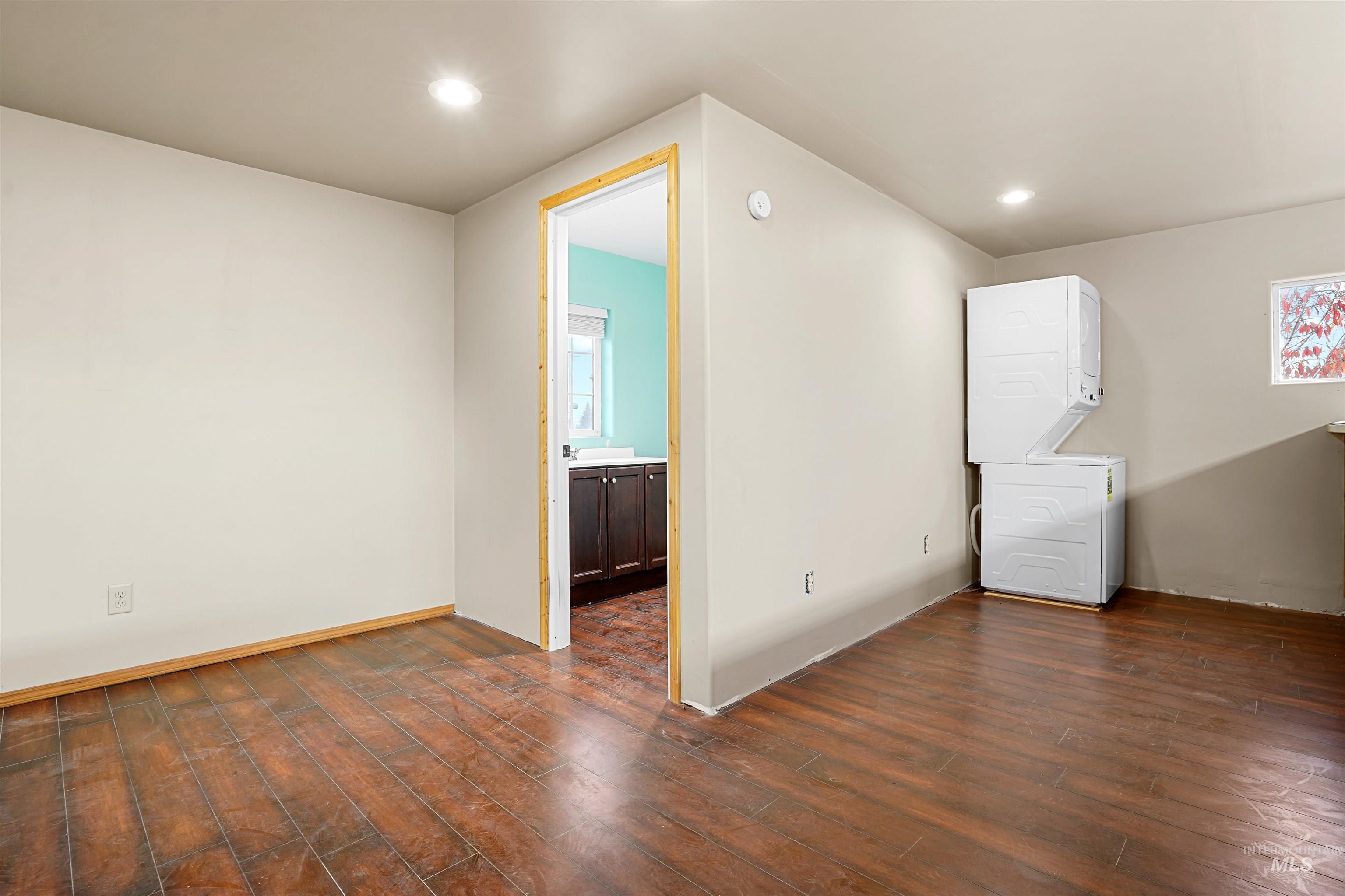 Spare room featuring stacked washer / drying machine, dark wood-type flooring, recessed lighting, and plenty of natural light