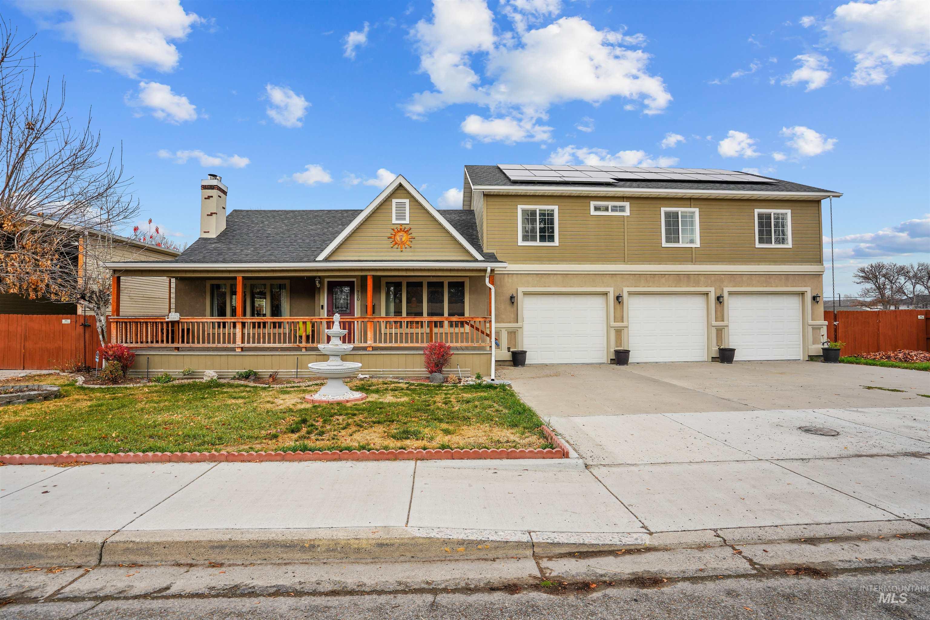 View of front of house featuring a porch, solar panels, concrete driveway, a chimney, and a garage