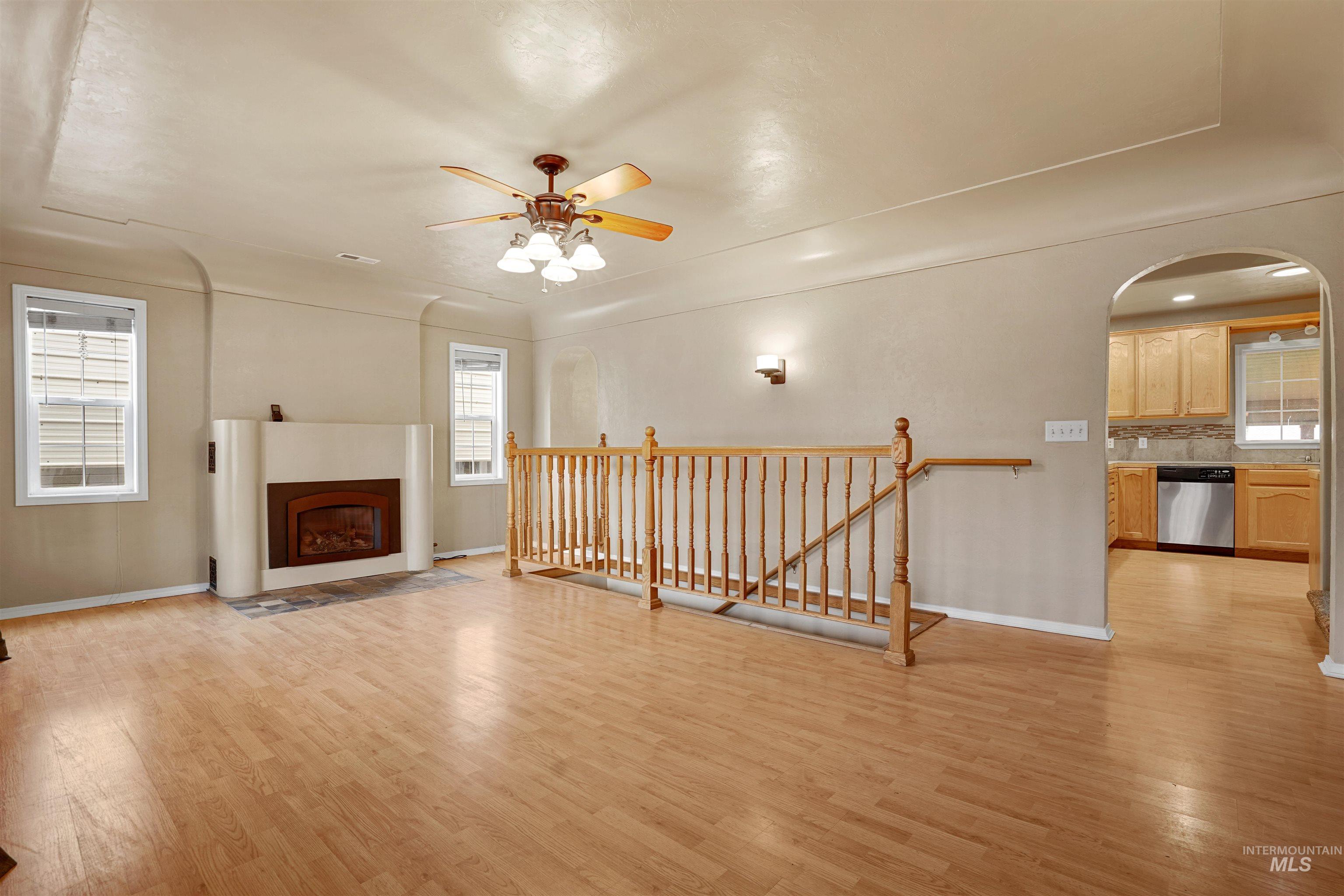 Unfurnished living room featuring light wood-style floors, a fireplace with flush hearth, ceiling fan, and arched walkways