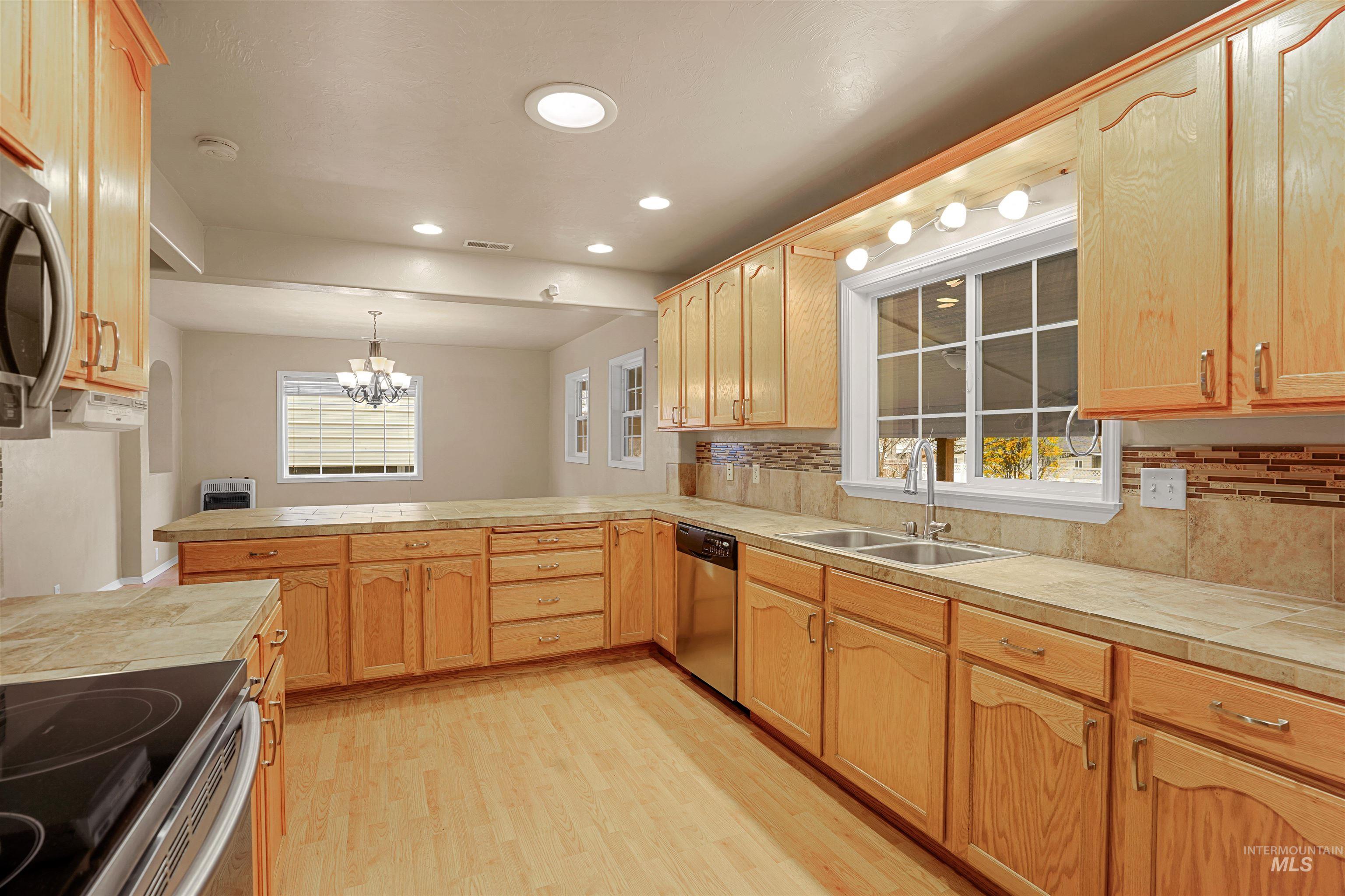 Kitchen featuring a peninsula, tile counters, light wood-style flooring, a chandelier, and plenty of natural light