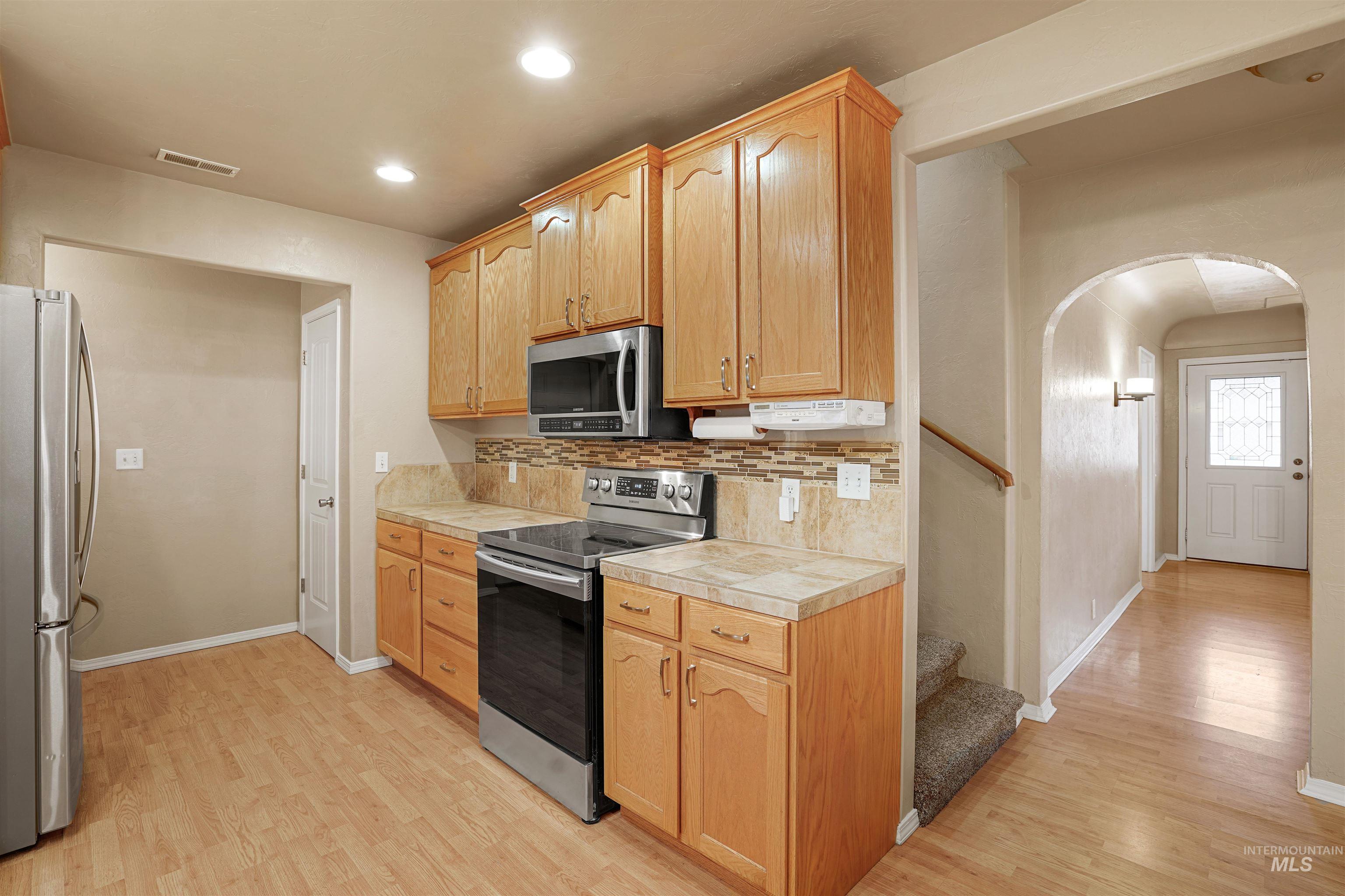 Kitchen featuring stainless steel appliances, arched walkways, light countertops, light wood-style flooring, and recessed lighting