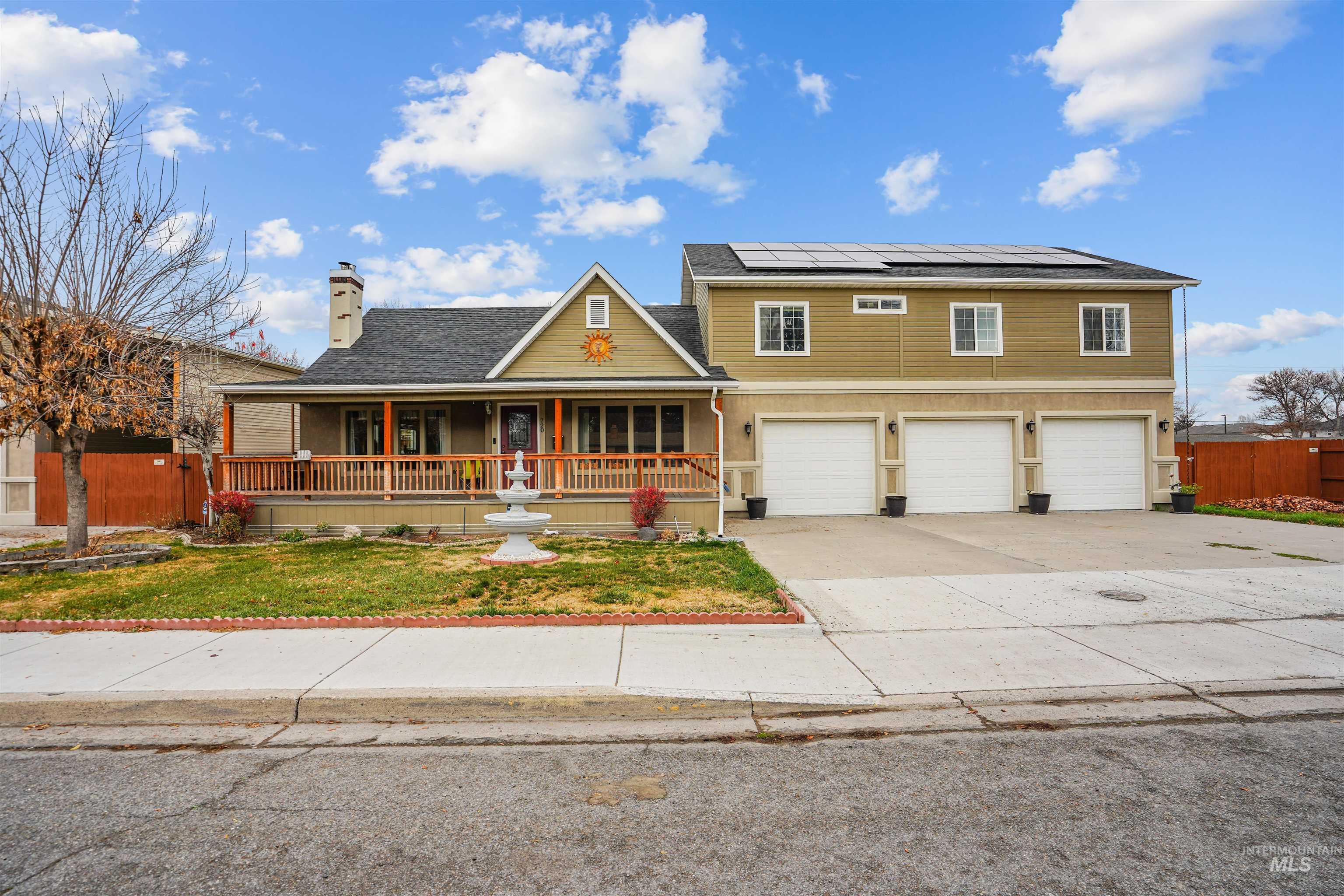 View of front of home with covered porch, driveway, roof mounted solar panels, a garage, and a chimney