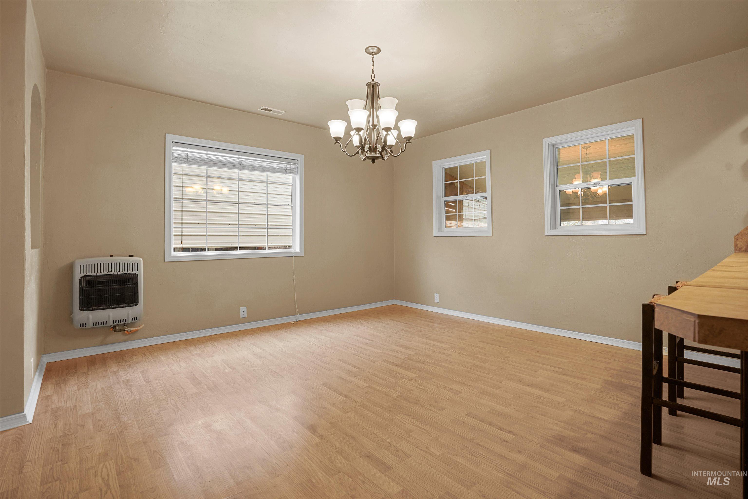 Unfurnished dining area featuring heating unit, light wood-style flooring, and a chandelier