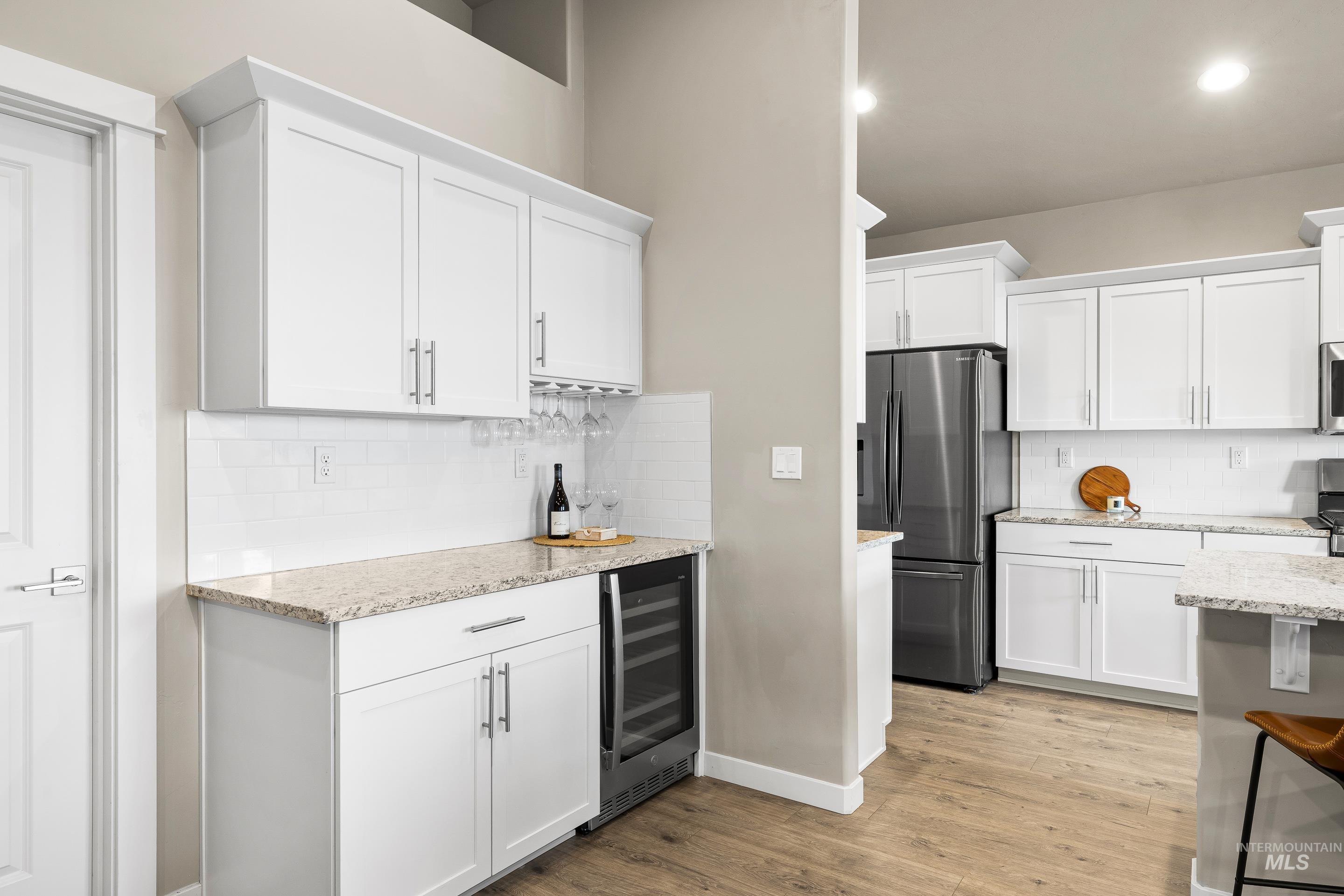 Kitchen featuring white cabinetry, light stone counters, freestanding refrigerator, and recessed lighting