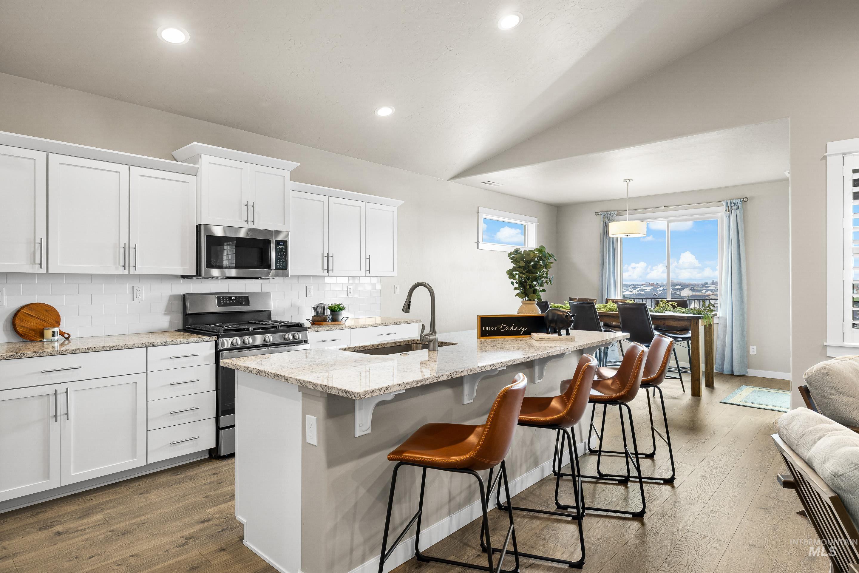 Kitchen with white cabinetry, stainless steel appliances, tasteful backsplash, light stone countertops, and vaulted ceiling