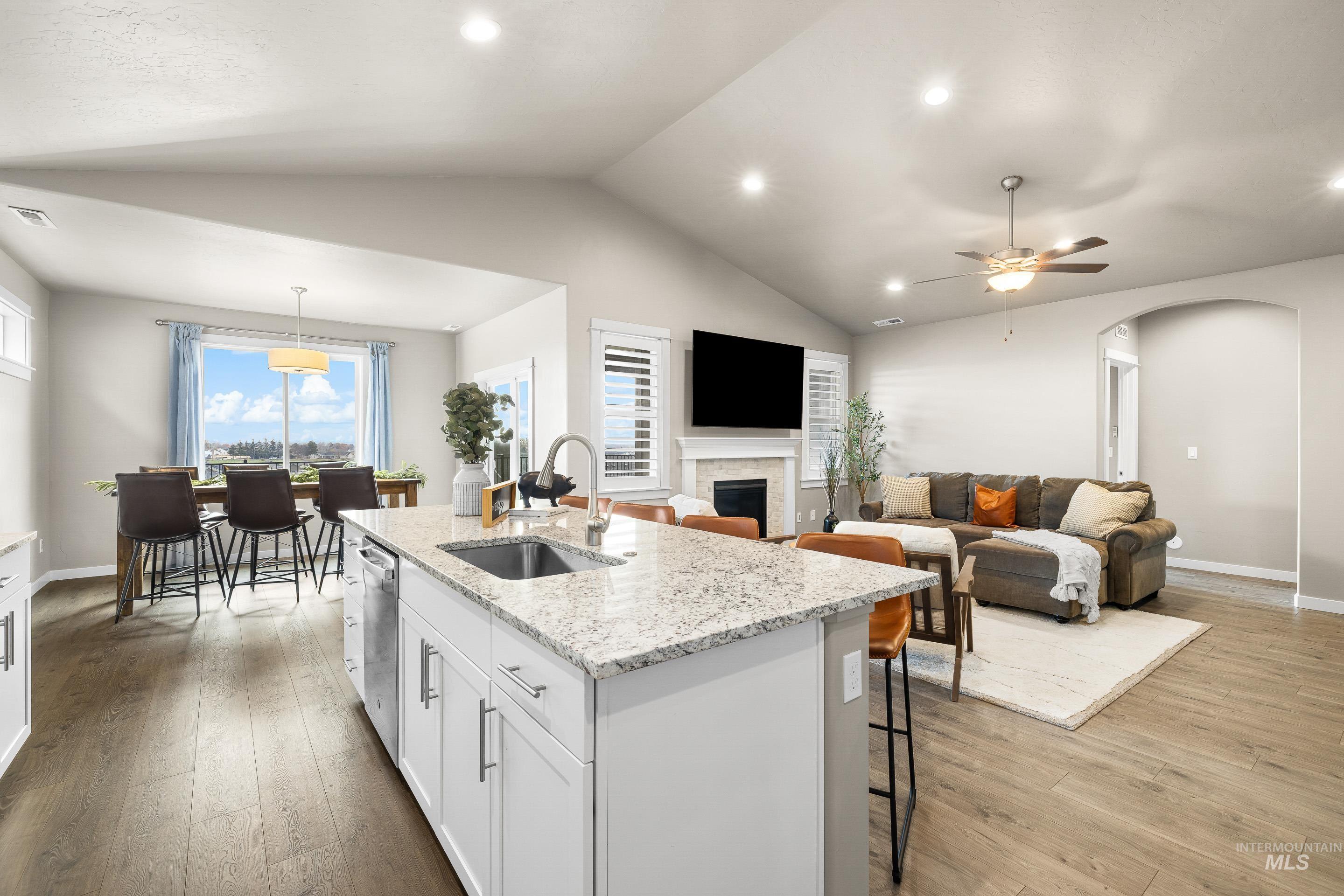 Kitchen featuring white cabinets, arched walkways, light wood-type flooring, light stone counters, and vaulted ceiling