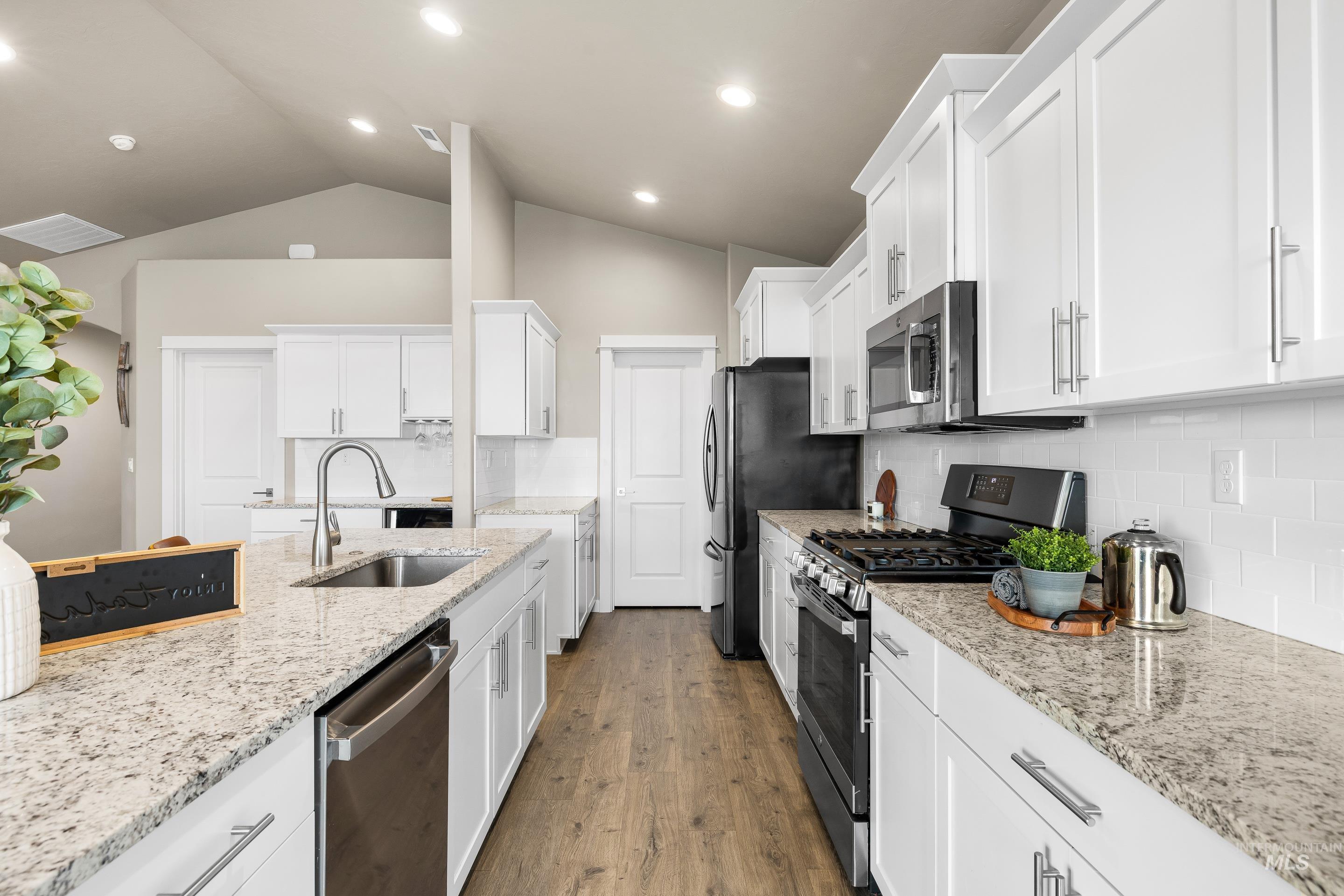 Kitchen featuring appliances with stainless steel finishes, white cabinetry, tasteful backsplash, light stone countertops, and dark wood finished floors