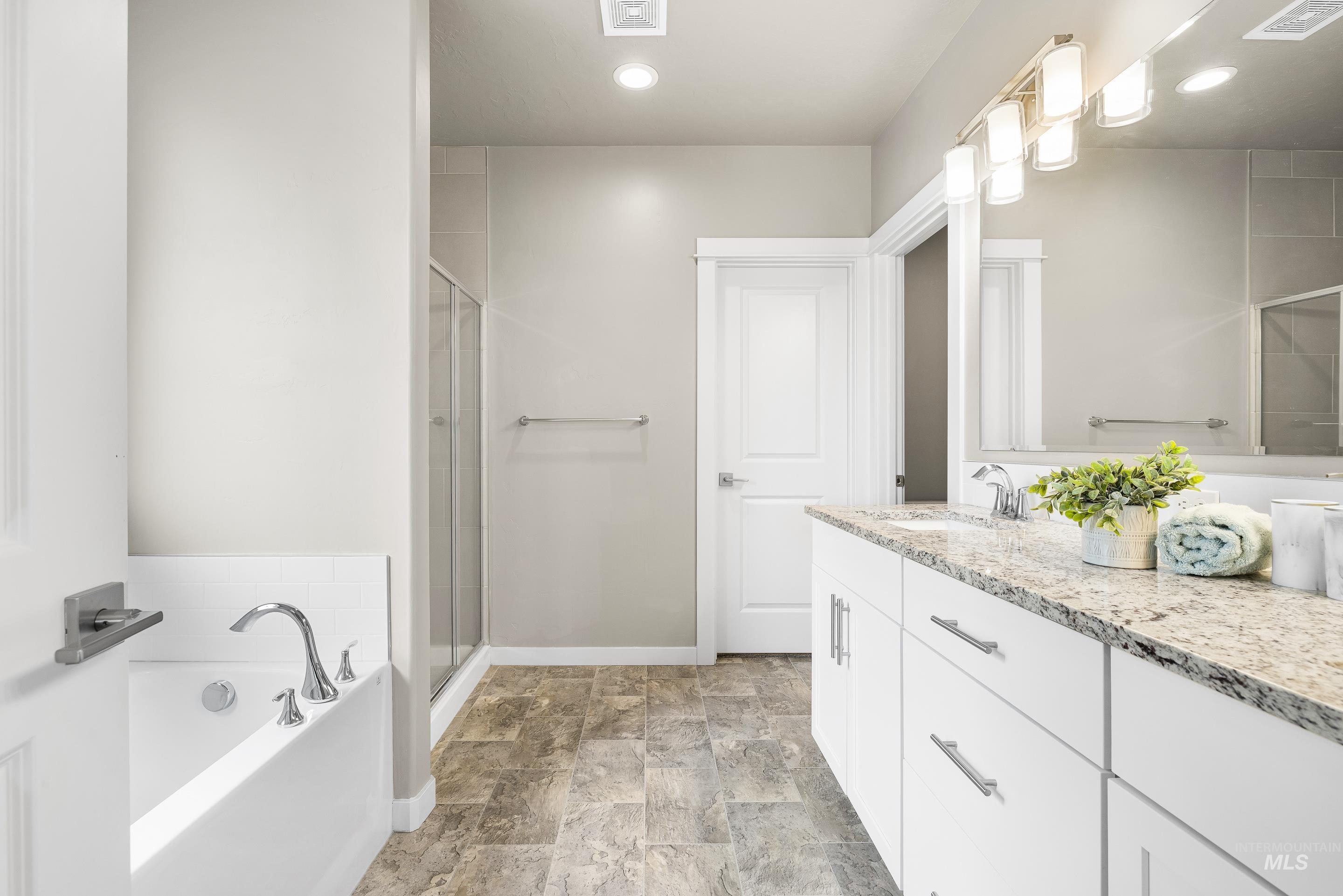 Full bathroom with double vanity, a garden tub, a shower stall, stone finish flooring, and recessed lighting