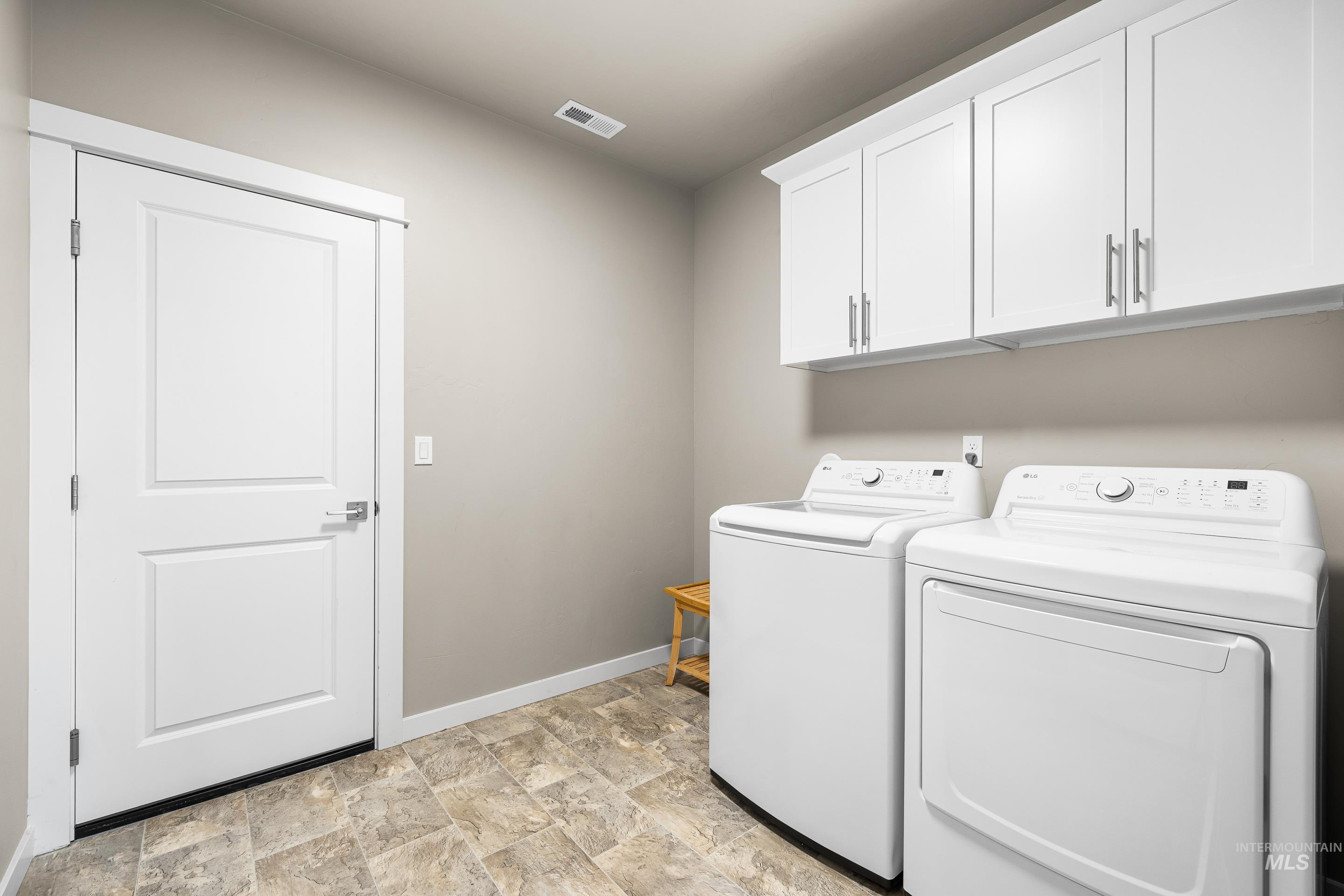 Washroom featuring washer and dryer, cabinet space, and stone finish flooring