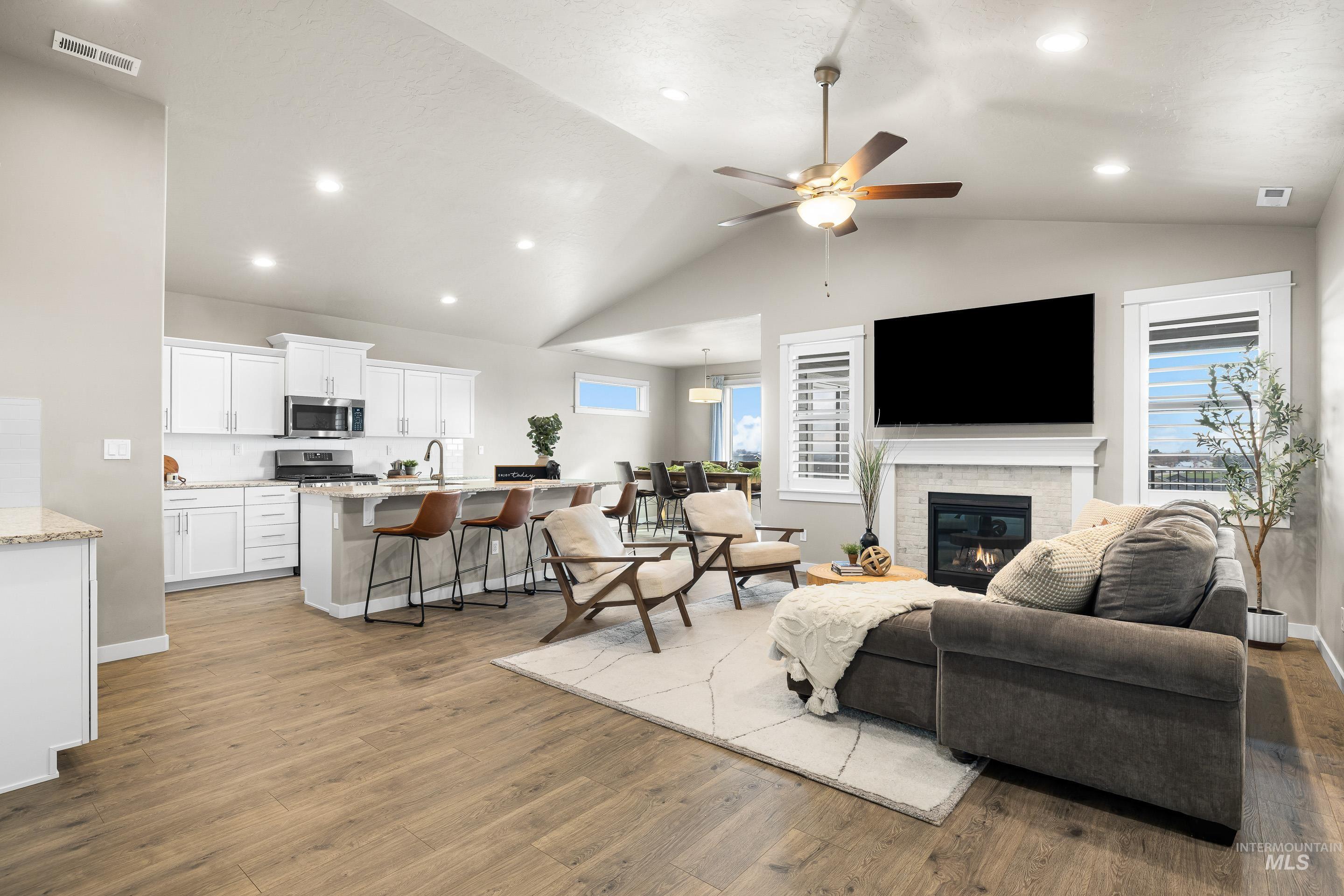 Living area featuring a ceiling fan, recessed lighting, light wood-style flooring, a glass covered fireplace, and high vaulted ceiling