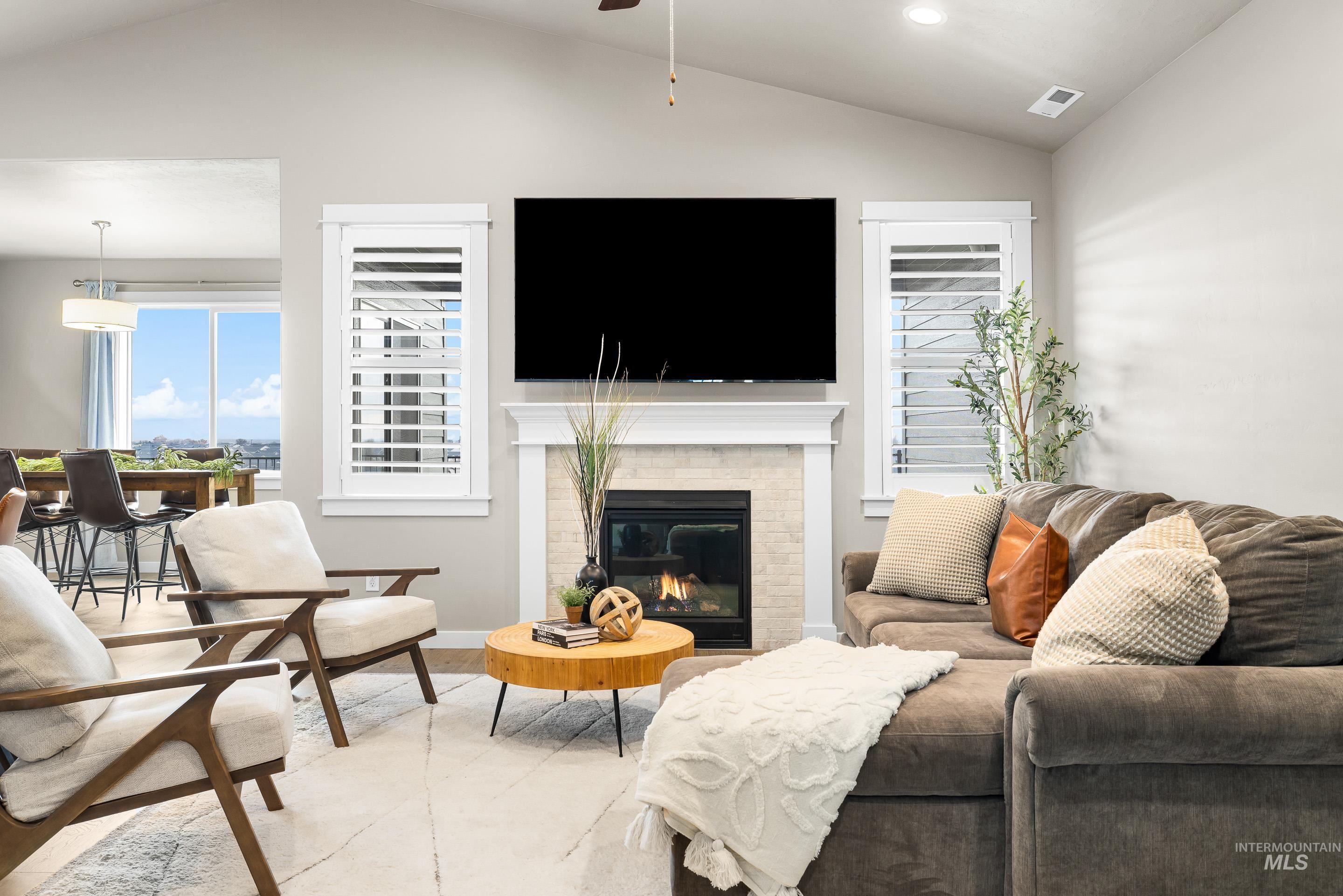 Living area featuring vaulted ceiling, a brick fireplace, and a ceiling fan