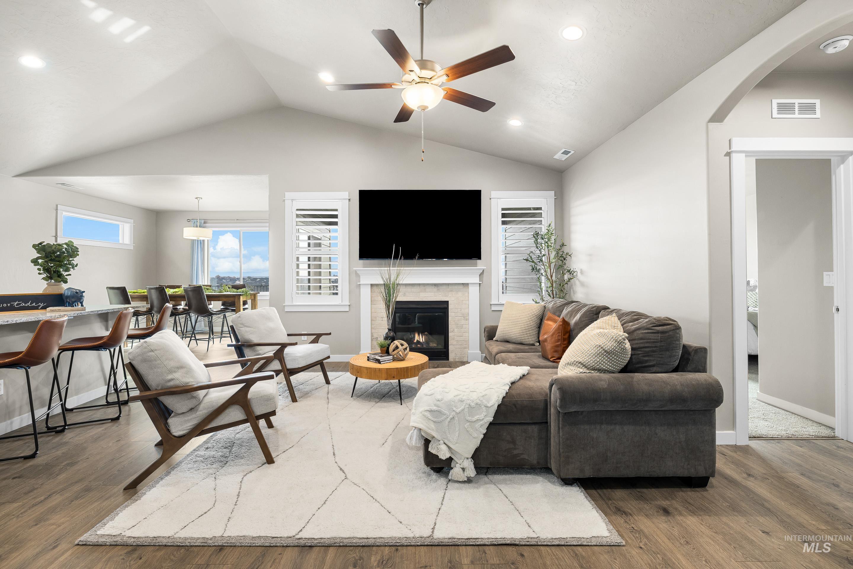 Living room featuring ceiling fan, vaulted ceiling, recessed lighting, a glass covered fireplace, and dark wood finished floors