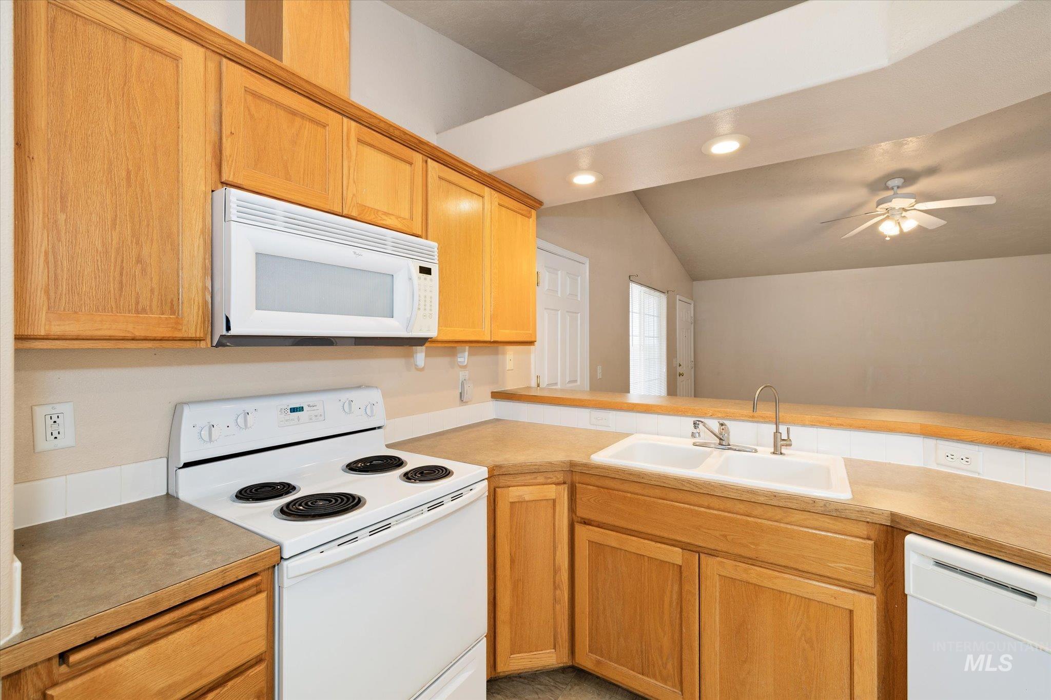 Kitchen featuring white appliances, vaulted ceiling, light countertops, ceiling fan, and recessed lighting