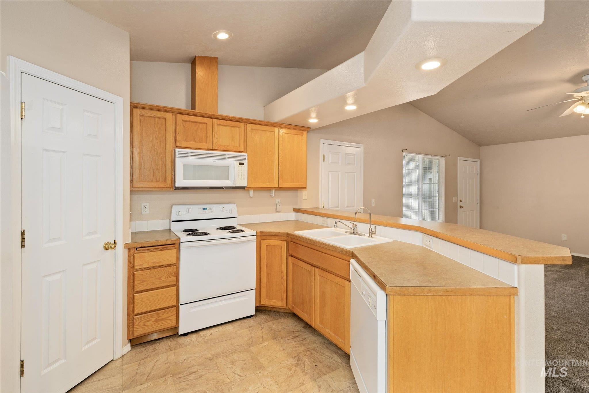 Kitchen with white appliances, a peninsula, light countertops, vaulted ceiling, and recessed lighting