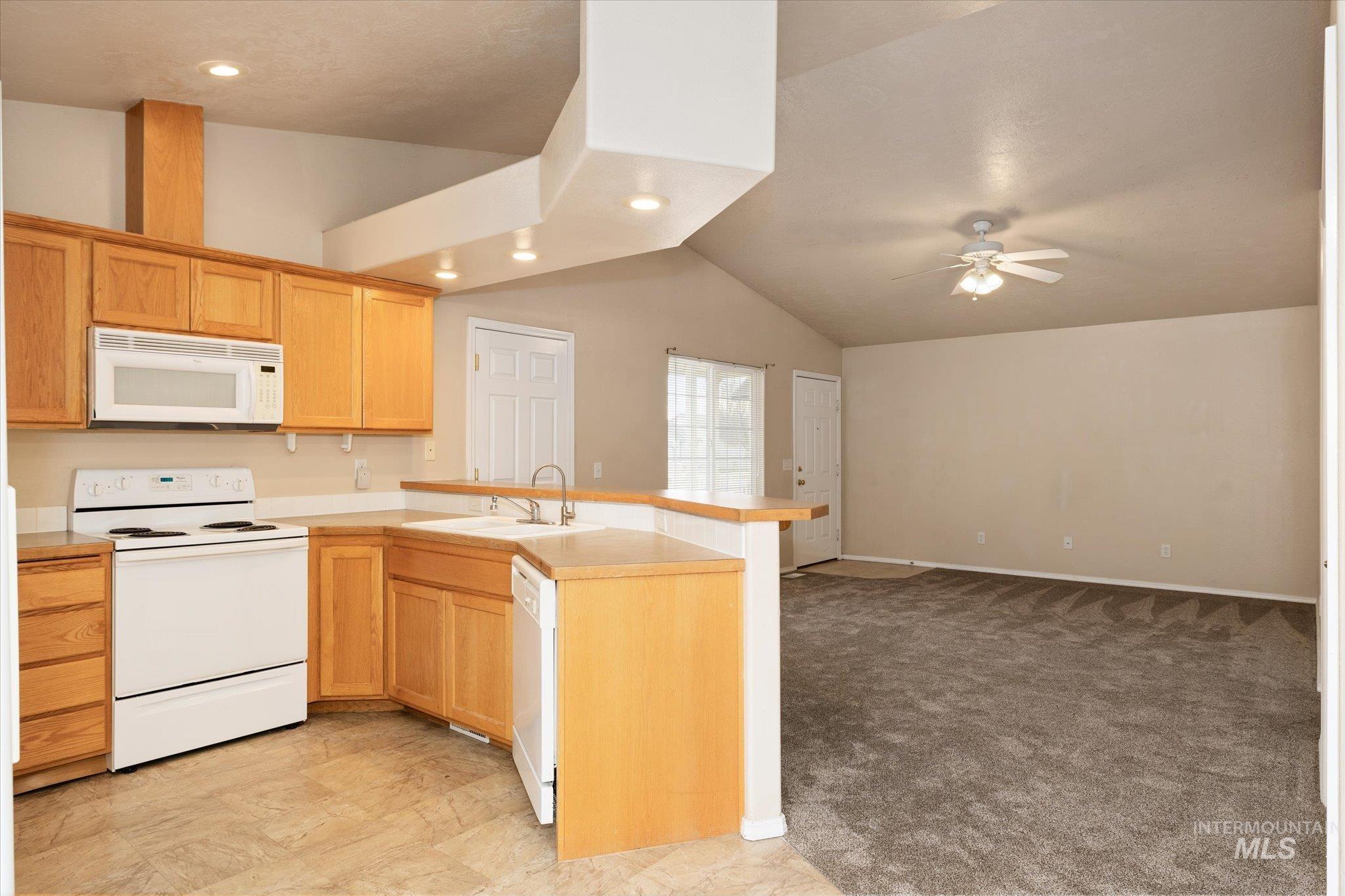 Kitchen featuring white appliances, a peninsula, lofted ceiling, open floor plan, and light colored carpet