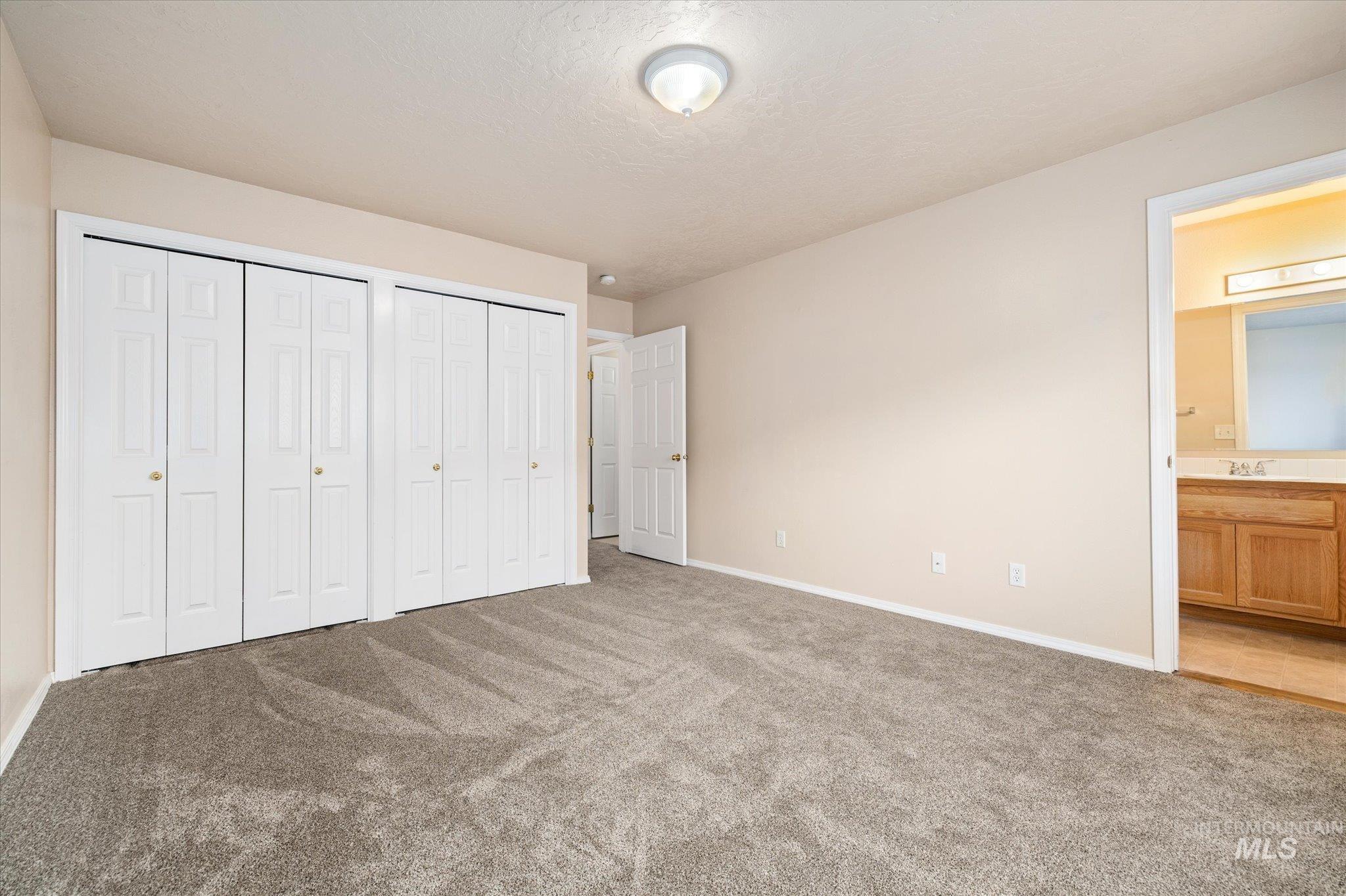 Unfurnished bedroom with light colored carpet, connected bathroom, two closets, and a textured ceiling