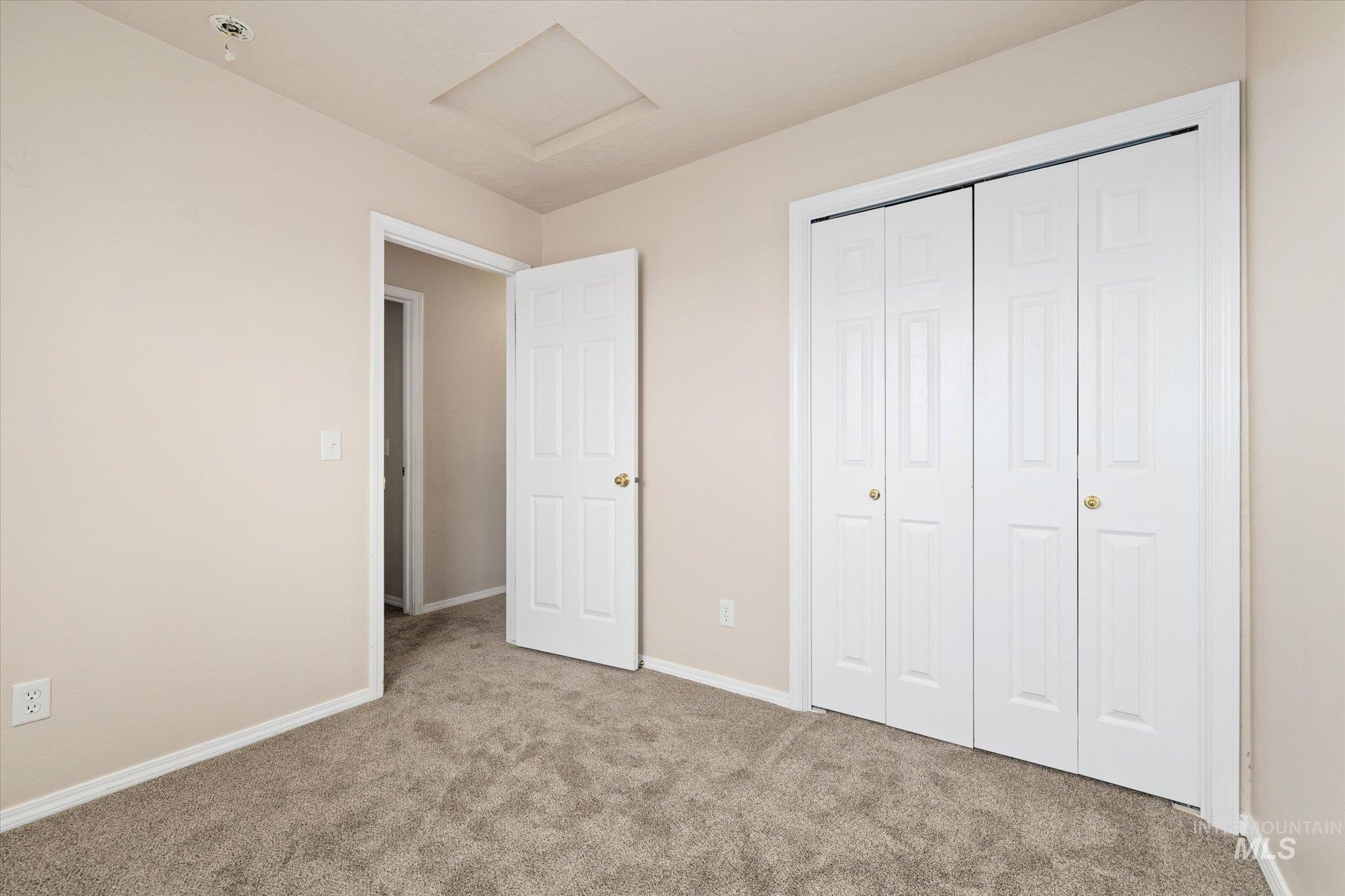 Unfurnished bedroom with attic access, carpet floors, and a closet