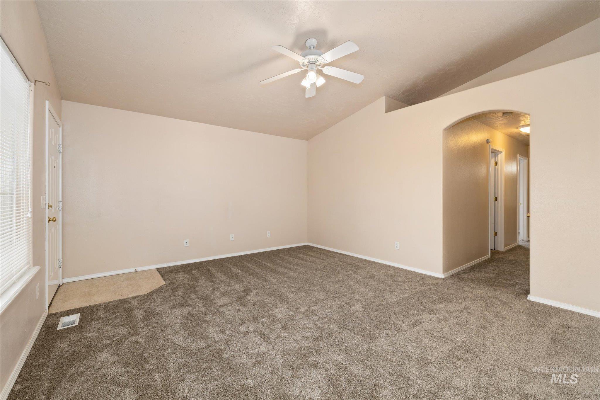 Empty room featuring lofted ceiling, arched walkways, a ceiling fan, and carpet