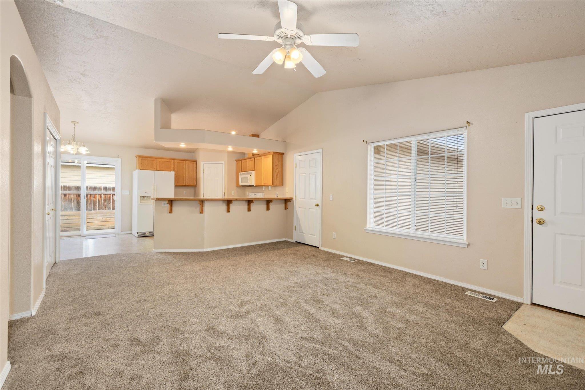 Unfurnished living room featuring lofted ceiling, ceiling fan, and light colored carpet