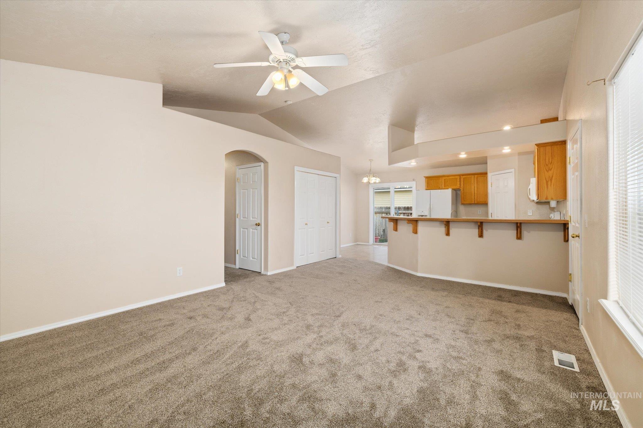 Unfurnished living room featuring vaulted ceiling, a ceiling fan, arched walkways, light colored carpet, and a chandelier