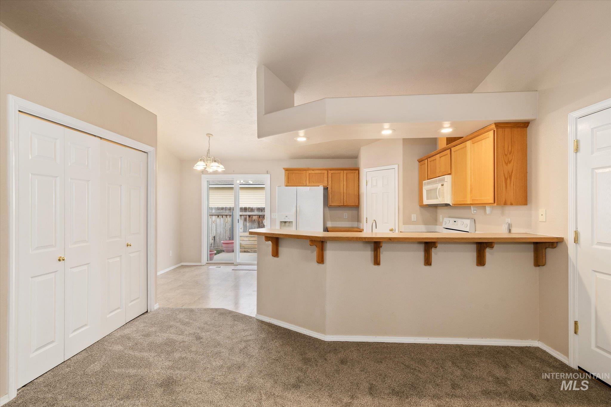 Kitchen featuring a chandelier, a peninsula, a breakfast bar, light countertops, and white appliances