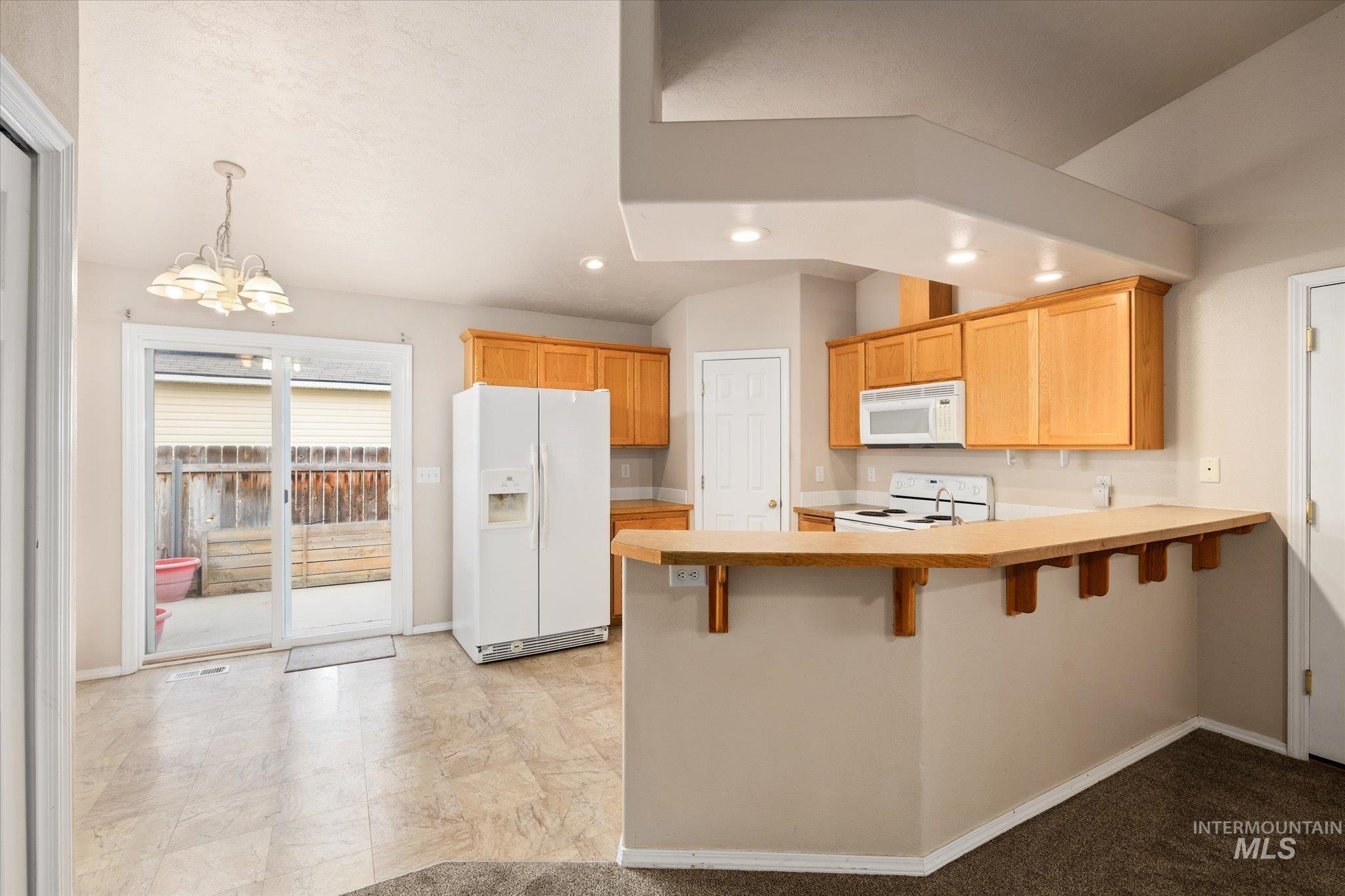 Kitchen featuring light countertops, white appliances, a peninsula, a chandelier, and a kitchen bar