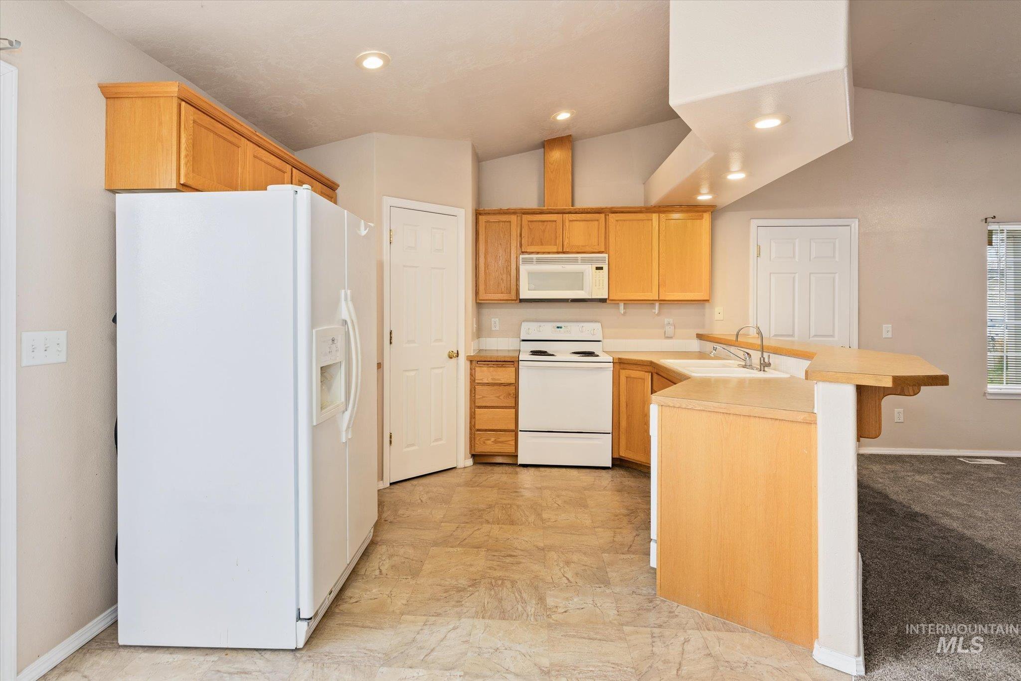 Kitchen featuring white appliances, a peninsula, light countertops, a breakfast bar area, and vaulted ceiling
