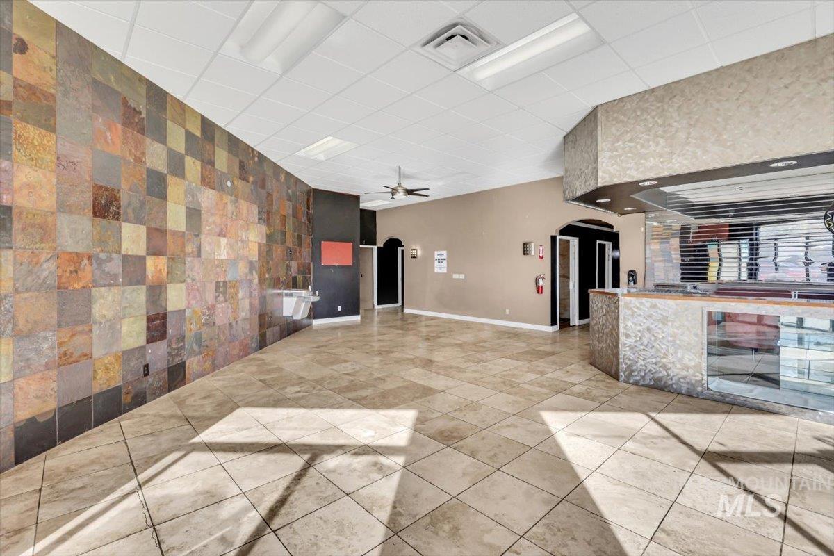 Unfurnished living room with arched walkways, an accent wall, ceiling fan, a paneled ceiling, and light tile patterned floors