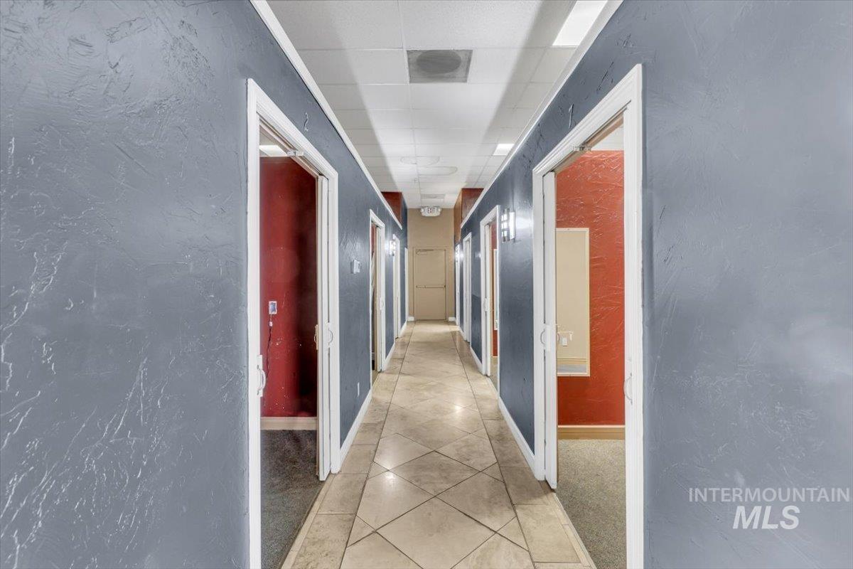 Hall with a textured wall, light tile patterned floors, and a paneled ceiling
