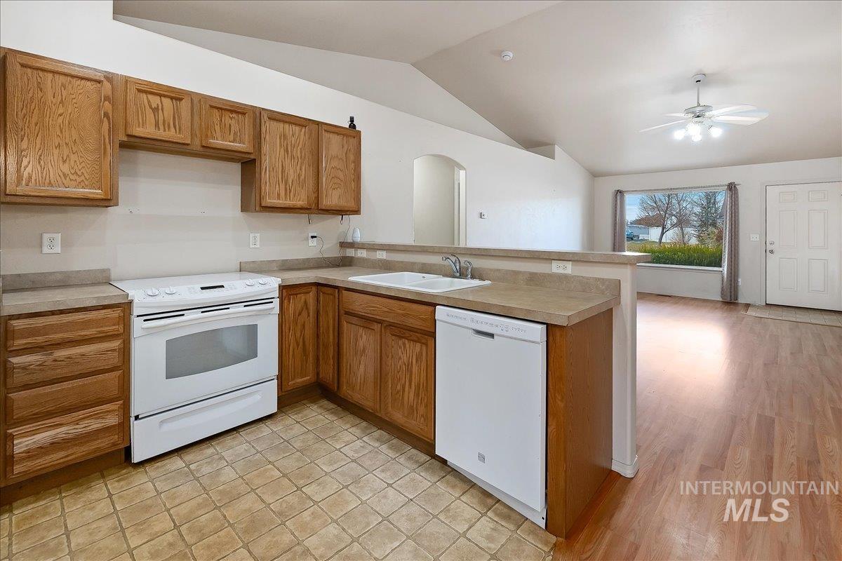 Kitchen with white appliances, brown cabinetry, a peninsula, lofted ceiling, and light countertops