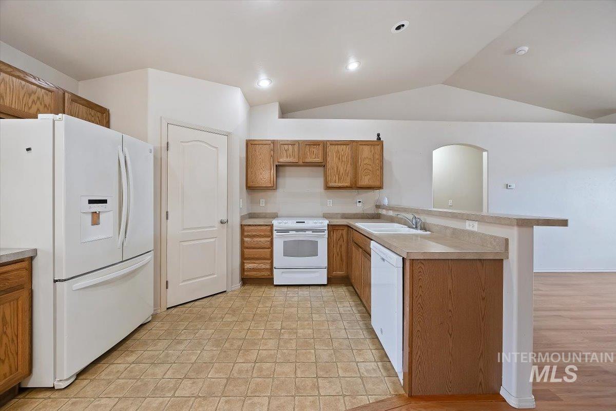 Kitchen featuring white appliances, a peninsula, light countertops, brown cabinets, and lofted ceiling