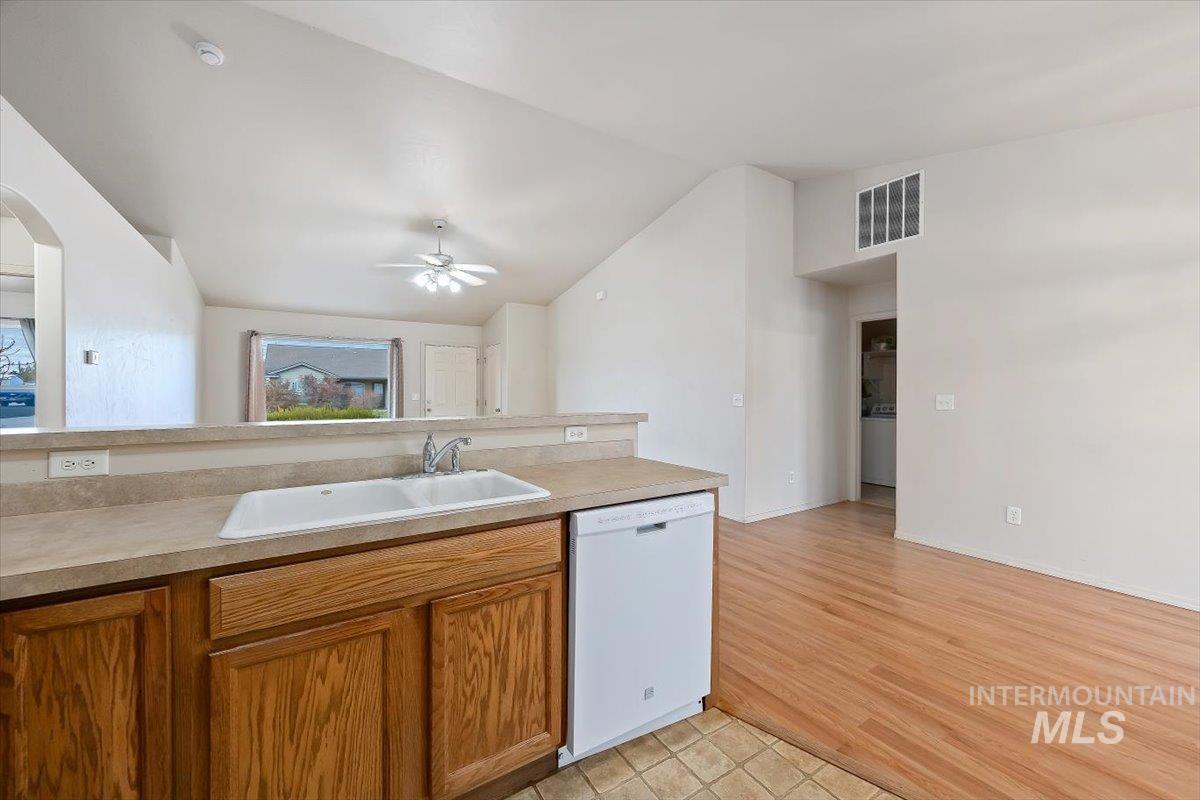 Kitchen featuring brown cabinets, dishwasher, vaulted ceiling, light countertops, and open floor plan