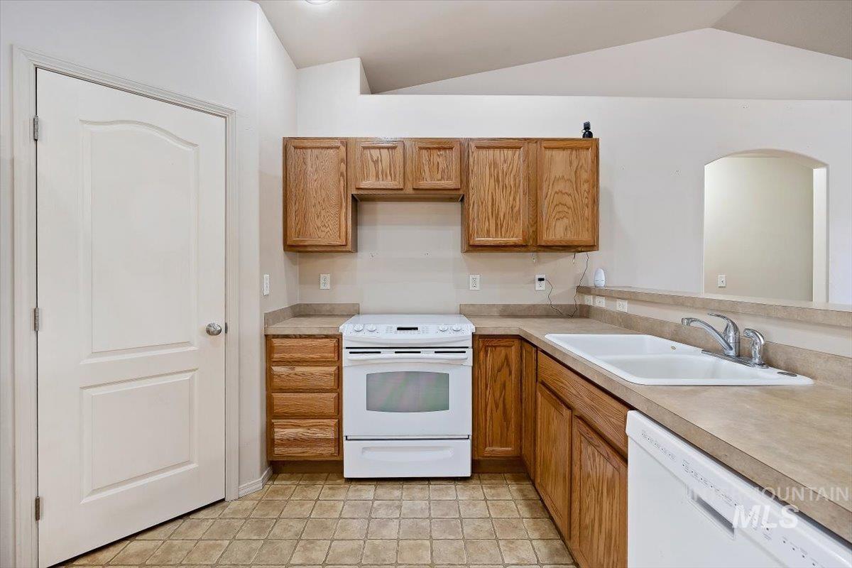 Kitchen featuring white appliances, light countertops, brown cabinetry, vaulted ceiling, and light tile patterned flooring
