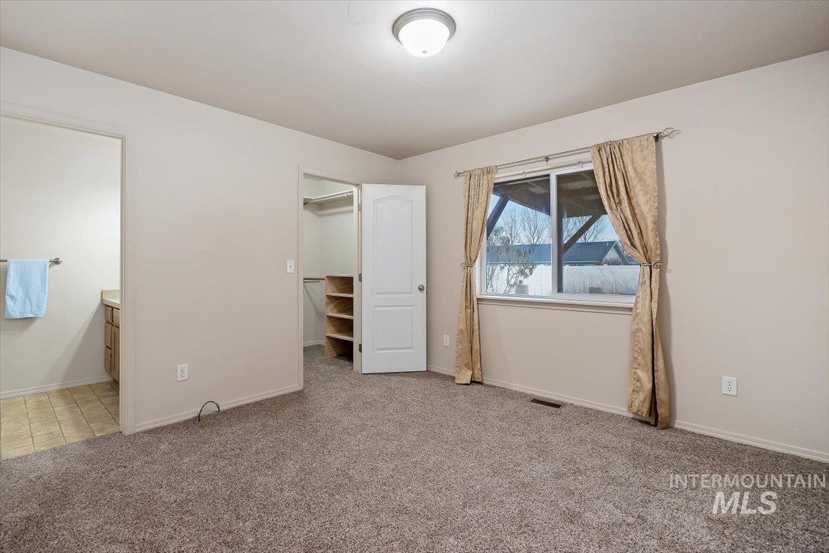 Unfurnished bedroom featuring a walk in closet, light colored carpet, and ensuite bathroom