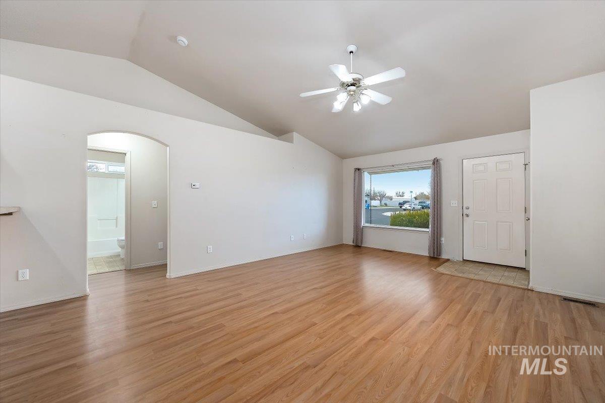 Unfurnished living room featuring vaulted ceiling, arched walkways, light wood-style flooring, and ceiling fan
