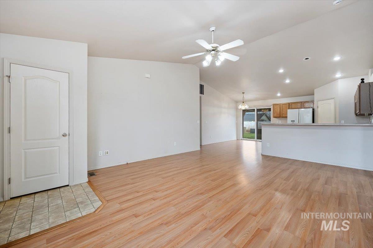 Unfurnished living room featuring lofted ceiling, light wood-style floors, a ceiling fan, recessed lighting, and a chandelier