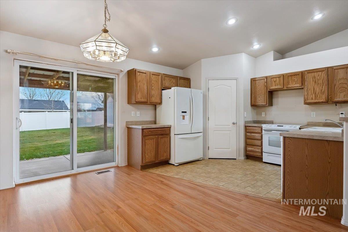 Kitchen featuring white appliances, brown cabinets, hanging light fixtures, light countertops, and vaulted ceiling