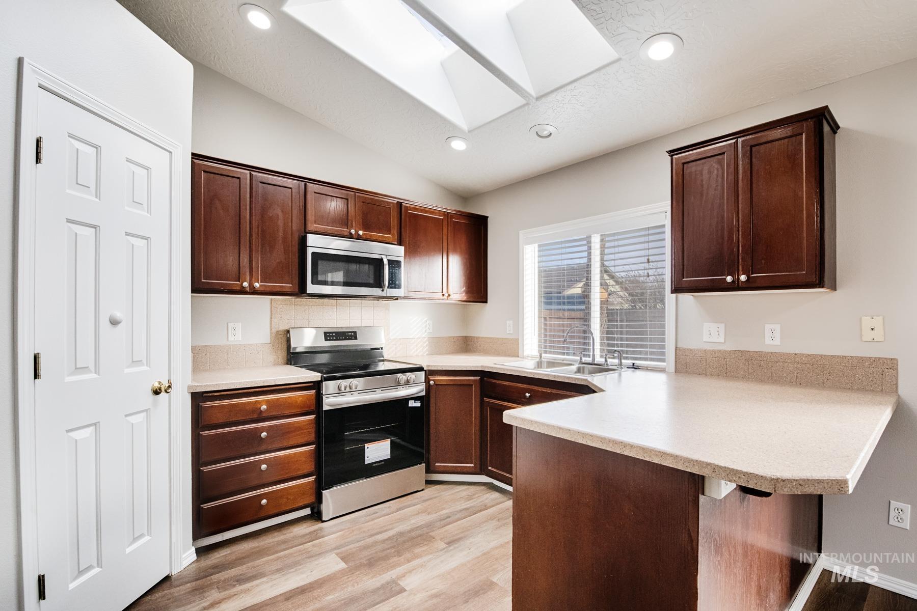 Kitchen with appliances with stainless steel finishes, light countertops, dark brown cabinets, a skylight, and lofted ceiling