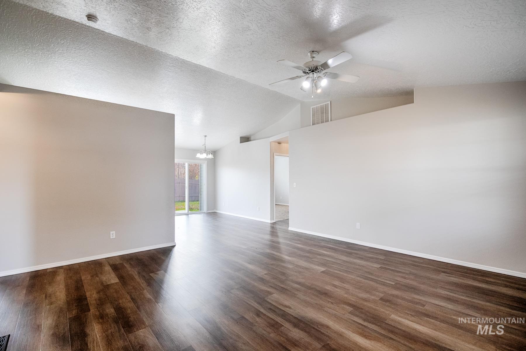 Spare room with dark wood finished floors, a chandelier, lofted ceiling, a ceiling fan, and a textured ceiling