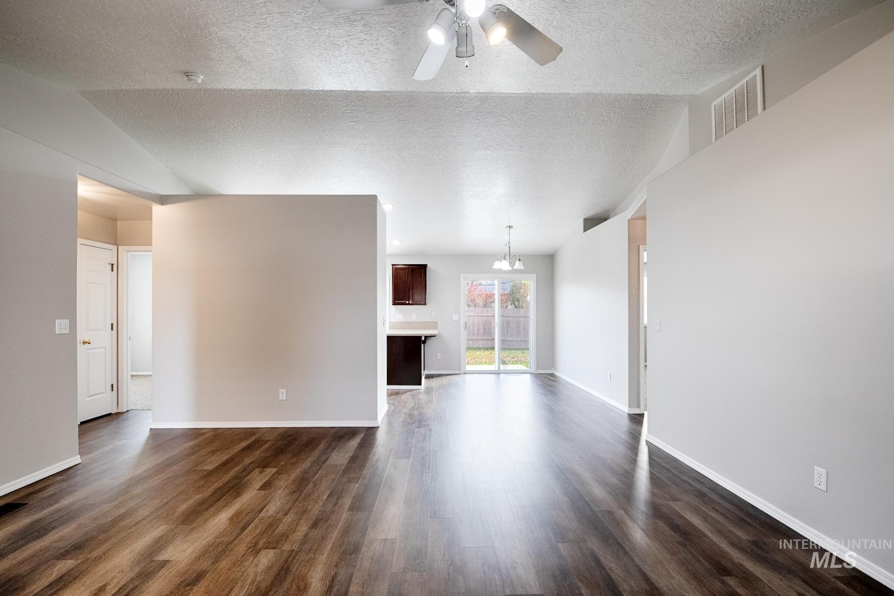 Unfurnished living room with dark wood-type flooring, a ceiling fan, and a textured ceiling