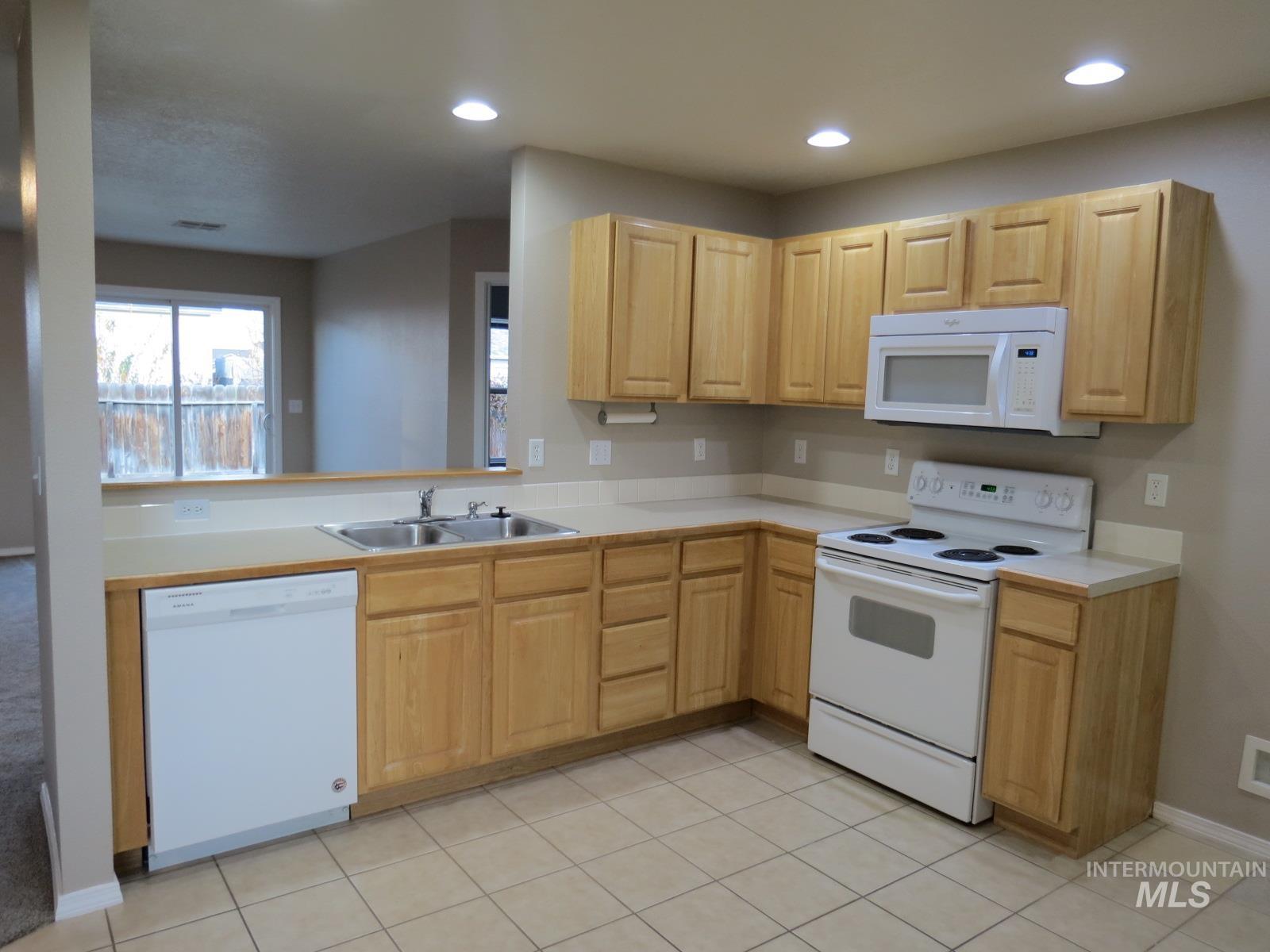 Kitchen featuring white appliances, light countertops, light brown cabinetry, recessed lighting, and a peninsula